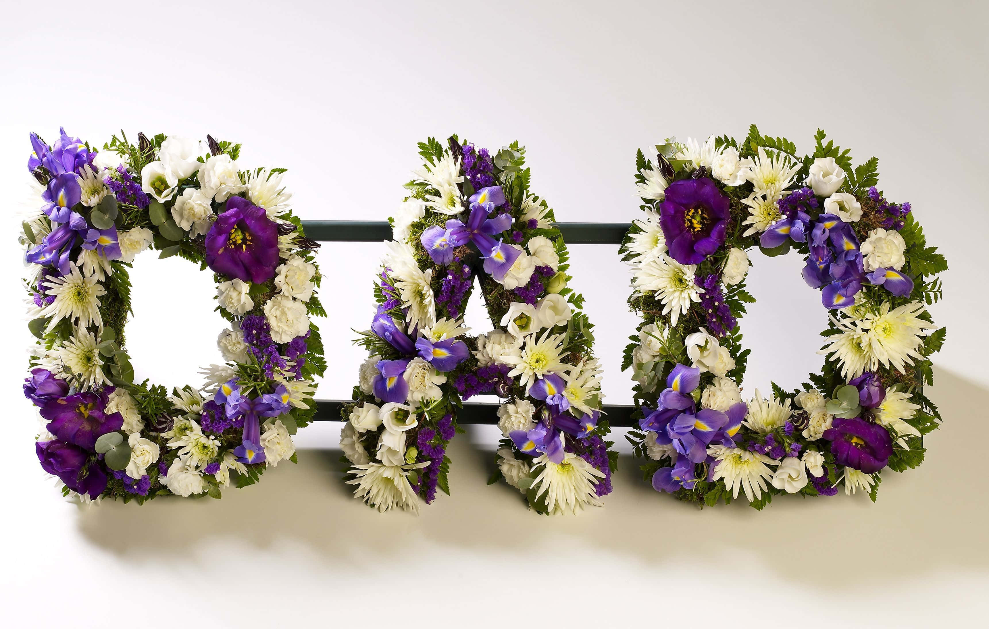 Funeral 桌布 壁紙 — 「DAD」這個字用大型花體字母拼寫，裝飾著紫色和白色的花朵及綠色植物，背景為純白色。