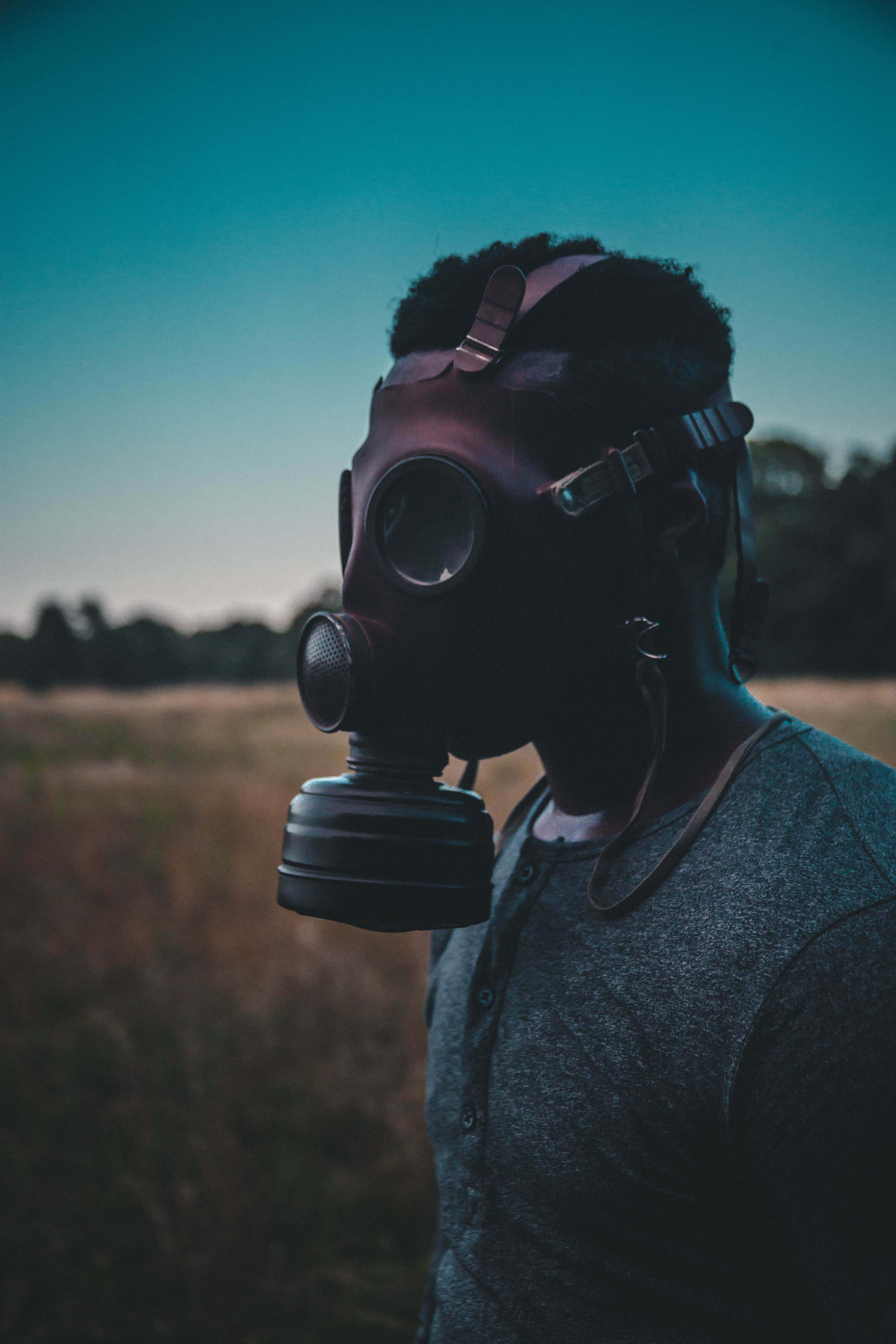 toxic 桌布 壁紙 — 一個戴著防毒面具的人站在田野中，天空呈現暮色，色調柔和，光線戲劇性。