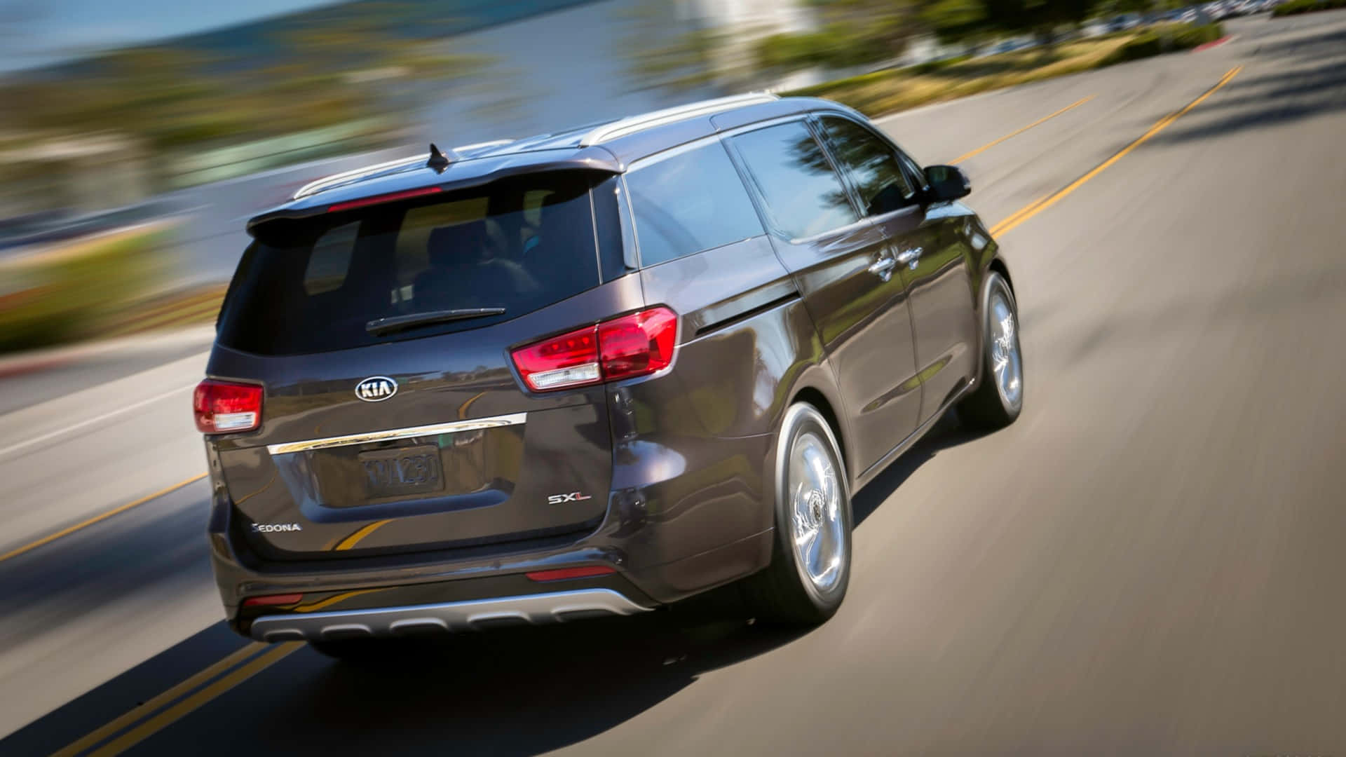 Kia Sedona 桌布 壁紙 — 一輛深灰色的Kia Sedona廂型車在陽光明媚的高速公路上疾馳，背景帶有動態模糊效果。