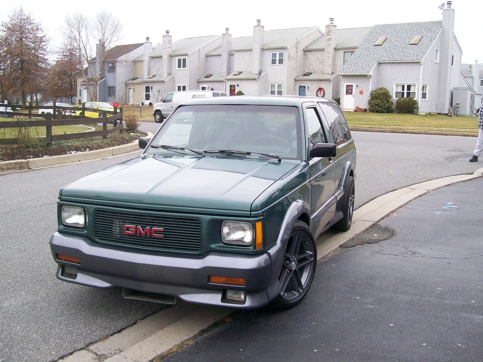Gmc Typhoon 桌布 壁紙 — 一輛深綠色GMC Jimmy SUV停放在住宅街道上，背景有郊區房屋和光禿禿的樹木。