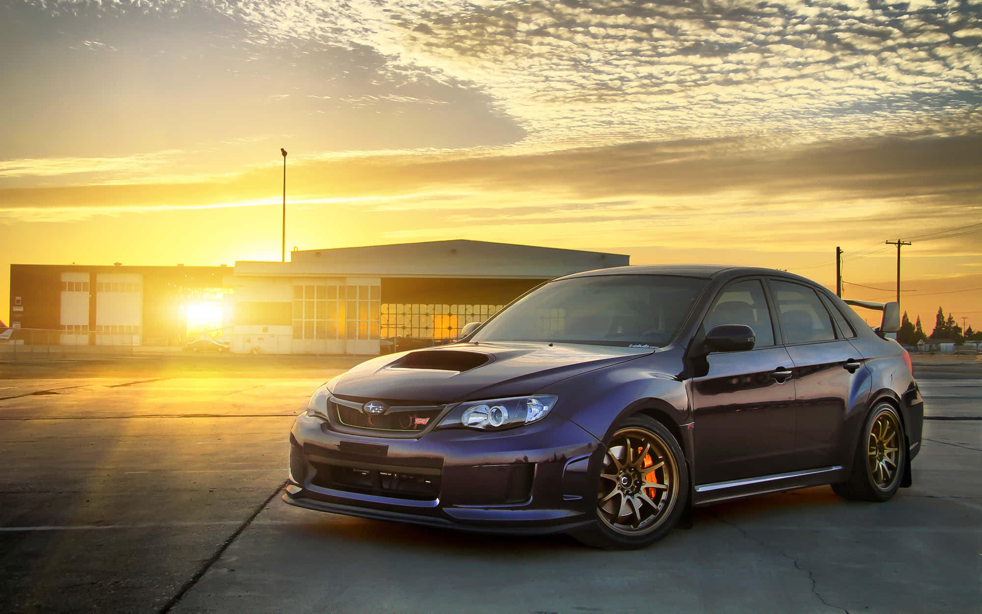 Subaru Impreza 桌布 壁紙 — 一架深紫色 Subaru WRX STI 停放在混凝土上，金色夕陽光芒沐浴著場景。