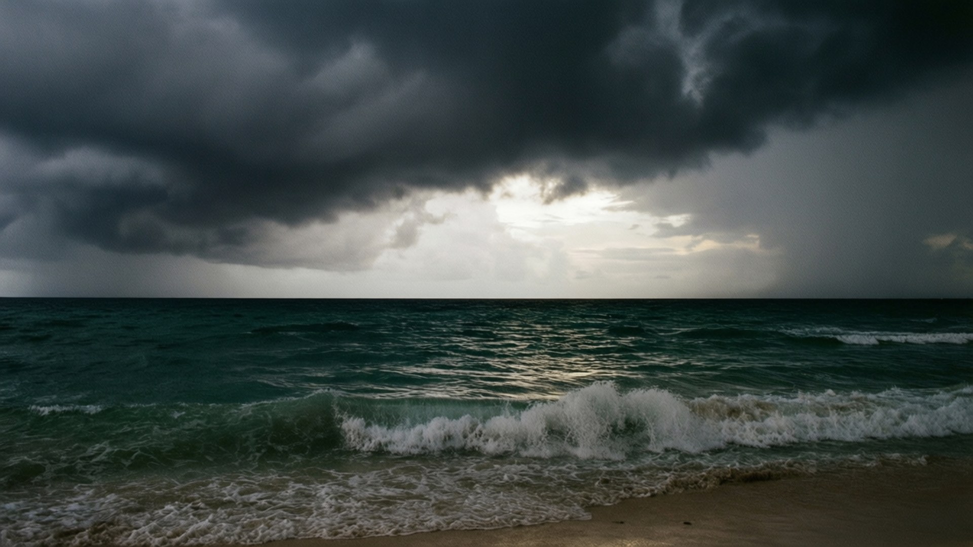 Storm Brewing at Jamaica Beach 壁紙 — 暗黑風暴雲籠罩著波濤洶湧的藍綠色海洋，拍打著沙灘，泛起白色泡沫。