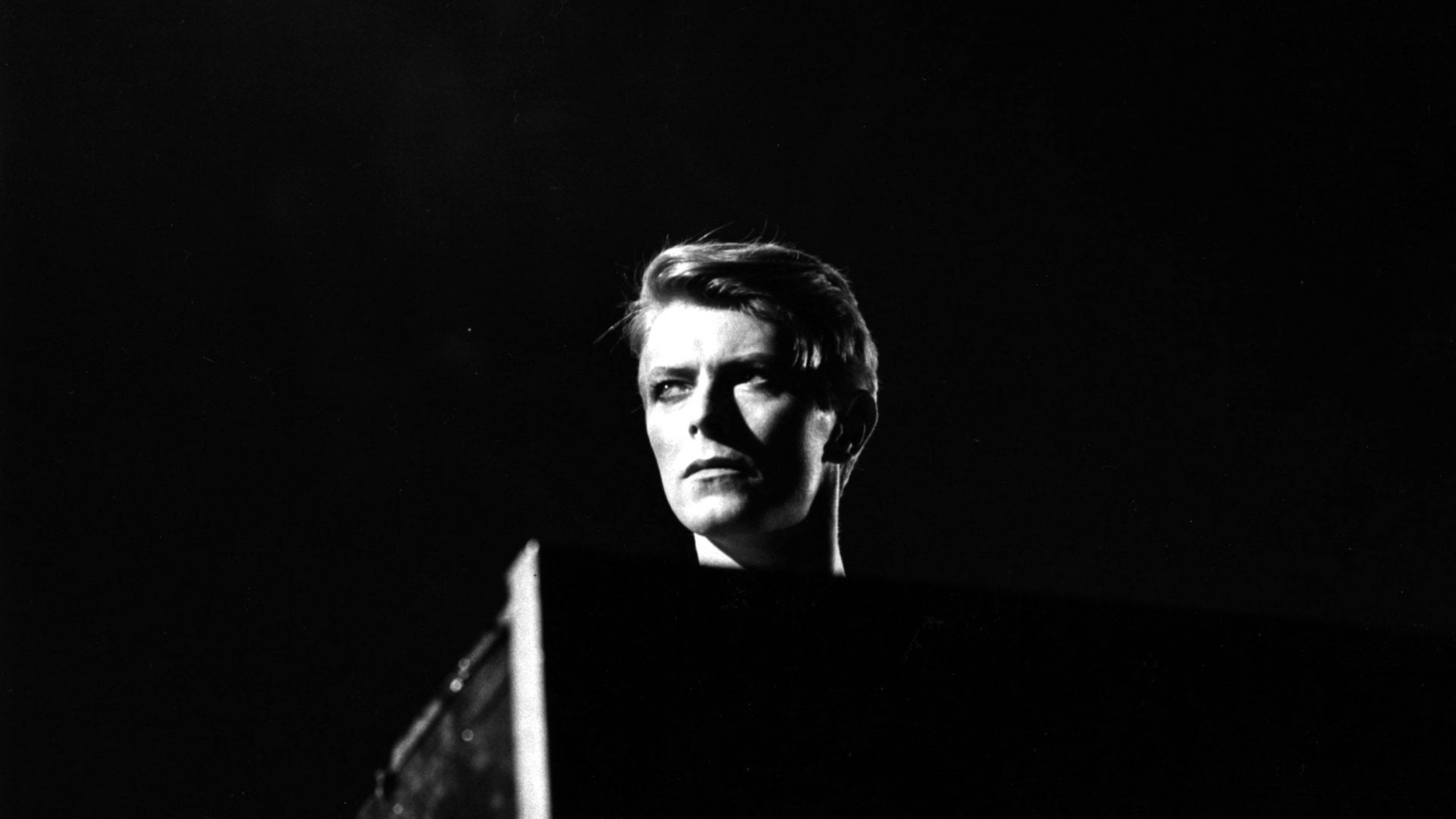 大衛·鮑伊 桌布 壁紙 — Davies Bowie 以高對比黑白呈現，戲劇性燈光，強烈凝視，背景深色。