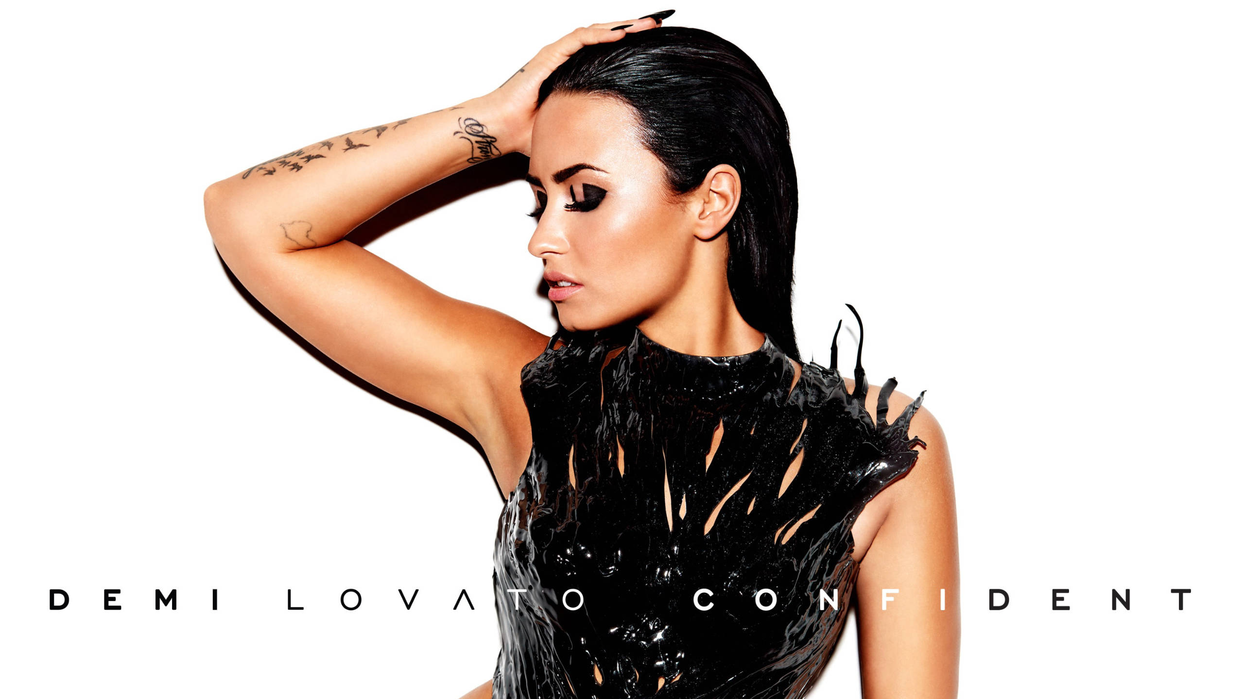 demi 桌布 壁紙 — Demi Lovato 在純白背景前，身穿亮黑色服裝，手放在頭髮上，自信地擺出姿勢。
