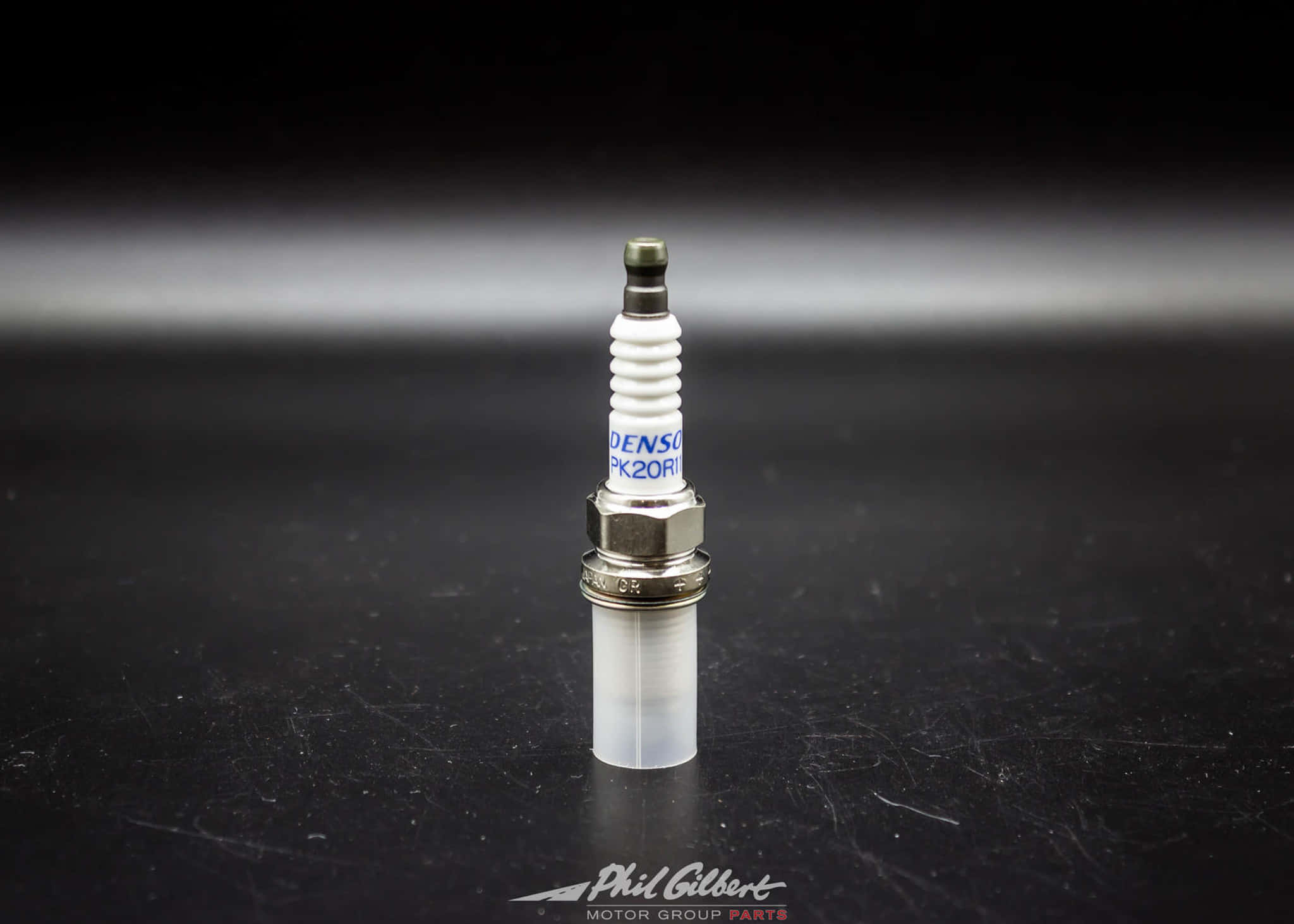 Spark Plug 桌布 壁紙 — Denso PK20R1 火星塞特寫，直立於有刮痕的黑色表面上，背景為模糊漸變色。
