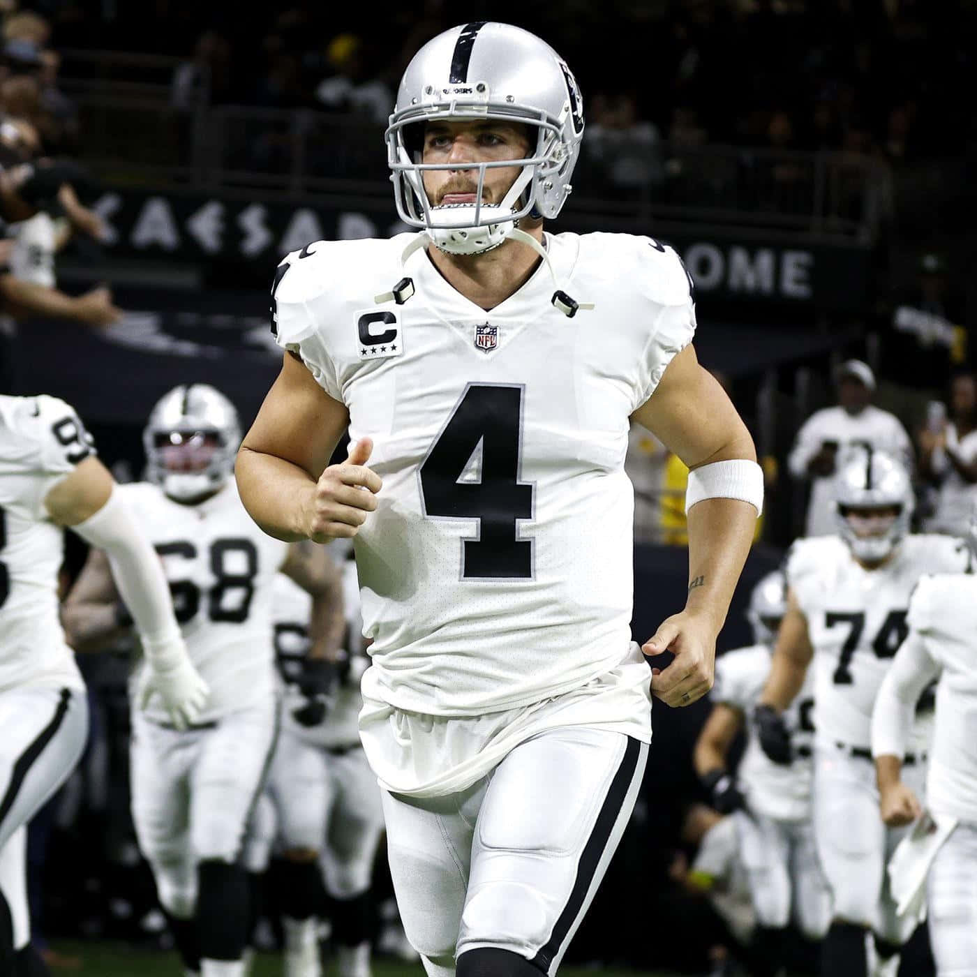  壁紙 — 一位決心堅定的NFL四分衛身穿白色球衣背號4，在夜間比賽的體育場燈光下衝刺過球場。