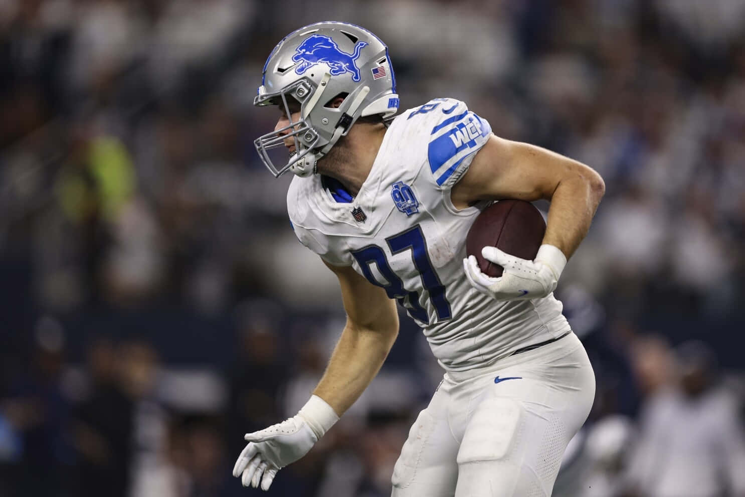  壁紙 — 一名身穿白色球衣的底特律雄獅美式足球員在夜間比賽中，於球場燈光下帶球衝刺。