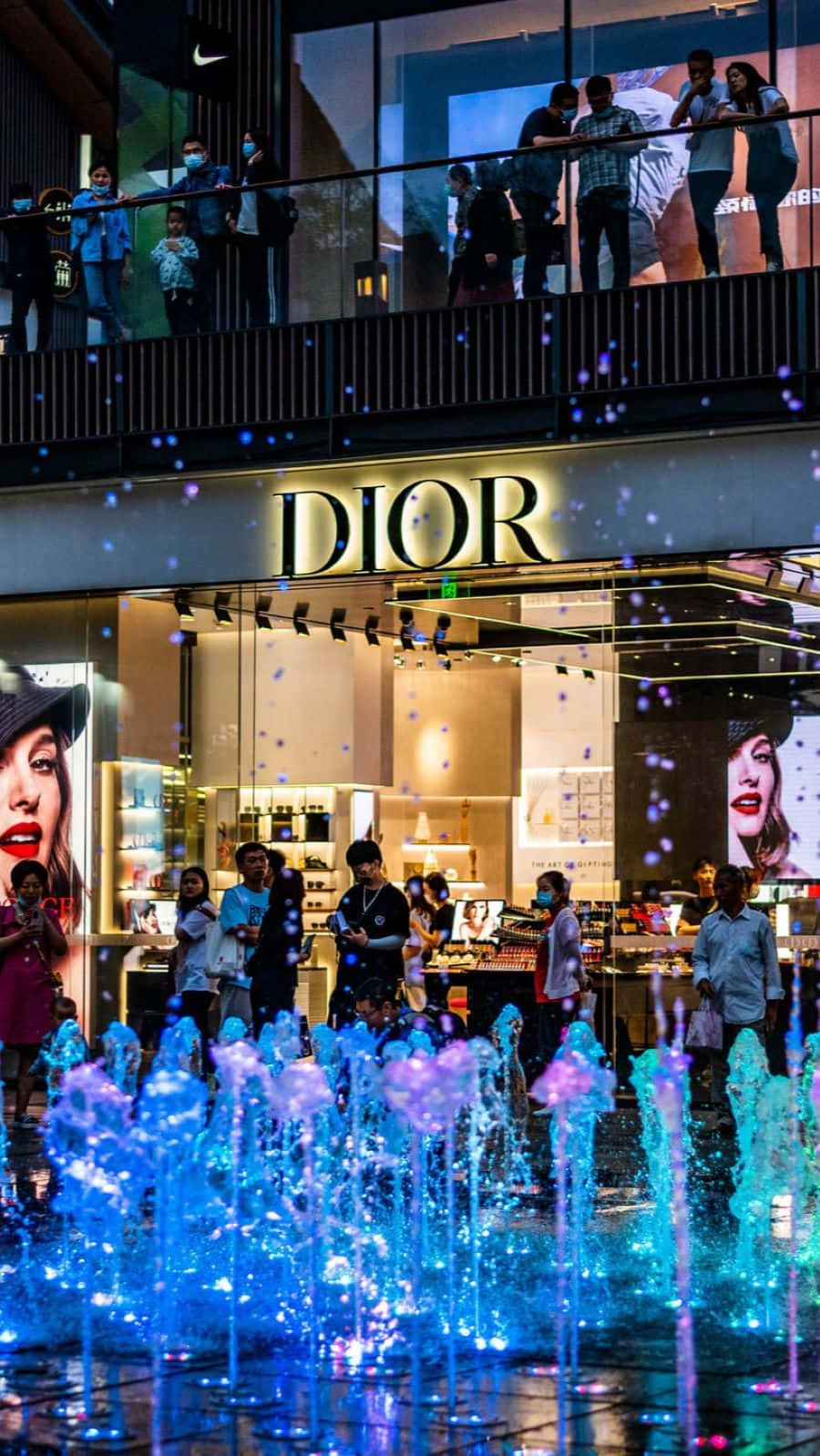  壁紙 — Dior 商店的迷人夜景，閃爍藍色噴泉和從上方觀看的人們。