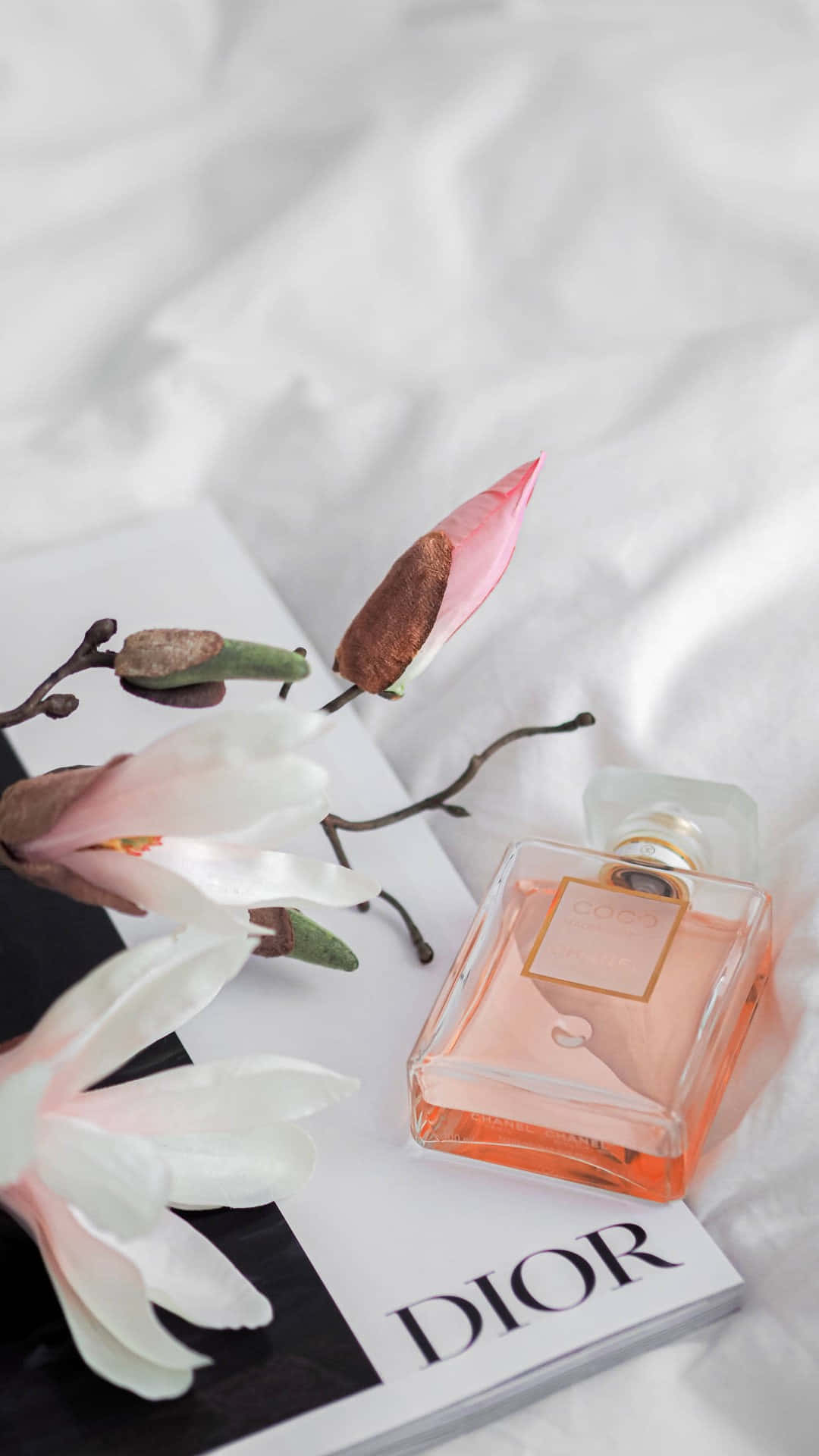  壁紙 — Dior 香水瓶放在柔軟白色布料上的雜誌上，旁邊有木蘭花。