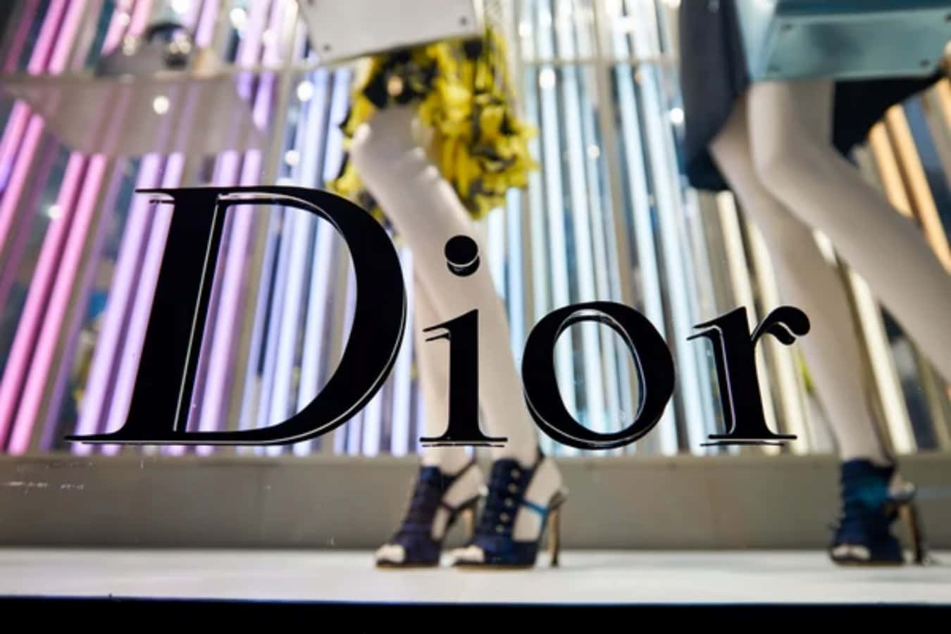 Dior 動態 桌布 壁紙 — Dior 標誌疊加在時尚的人體模型展示上，配有高跟鞋和色彩繽紛的垂直燈光，位於豪華商店櫥窗中。