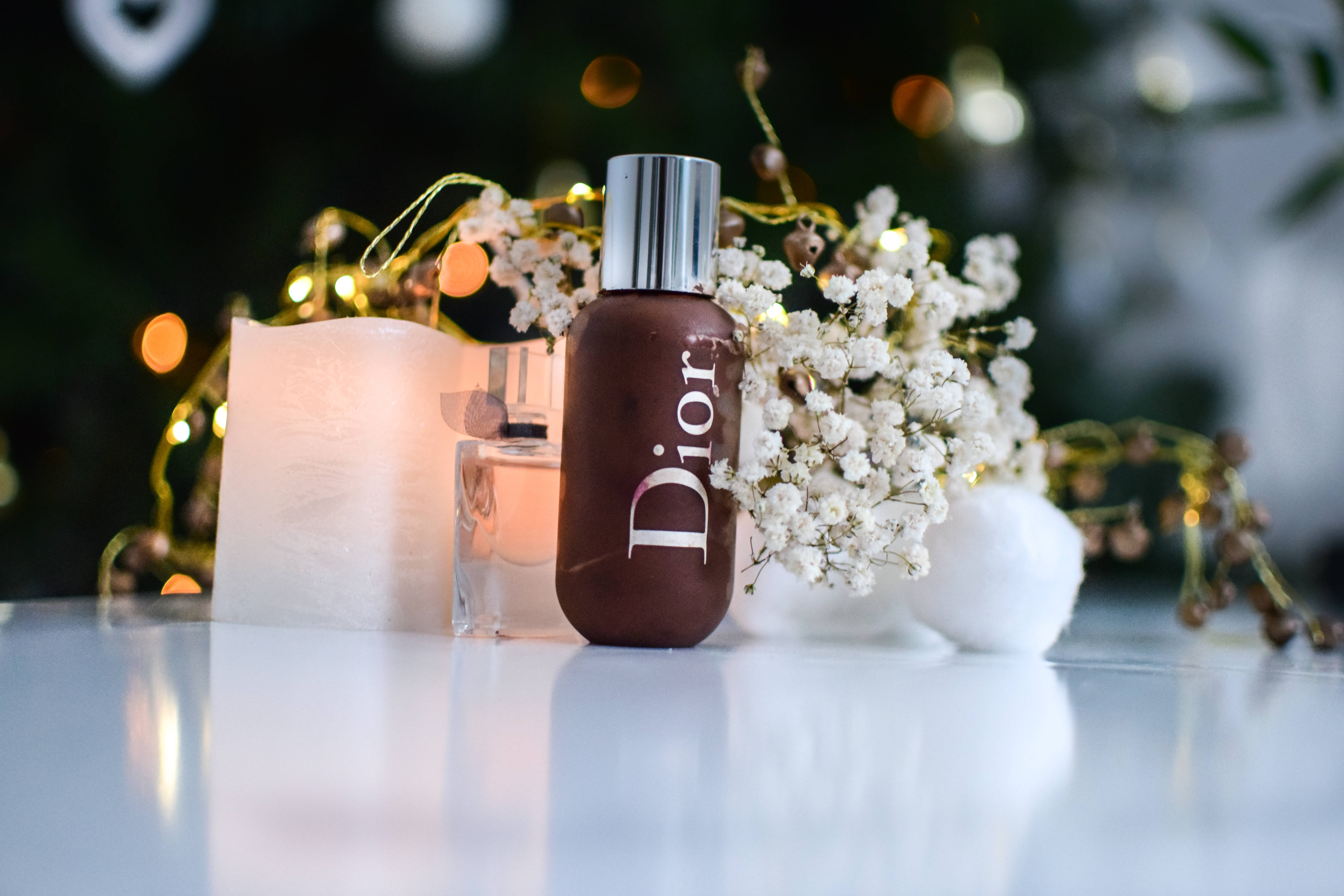 Dior 動態 桌布 壁紙 — Dior 香水瓶優雅地放在點燃的蠟燭和滿天星旁邊，背景是散景燈光的節日氛圍。