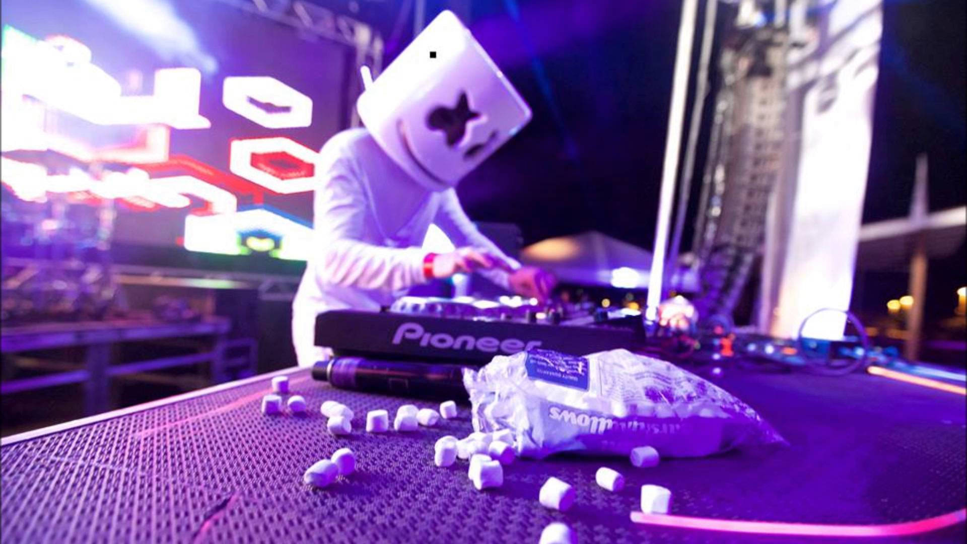 Marshmello 動態圖 桌布 壁紙 — DJ Marshmello 在夜間於充滿活力的紫色燈光下表演，桌上散落著迷你棉花糖。