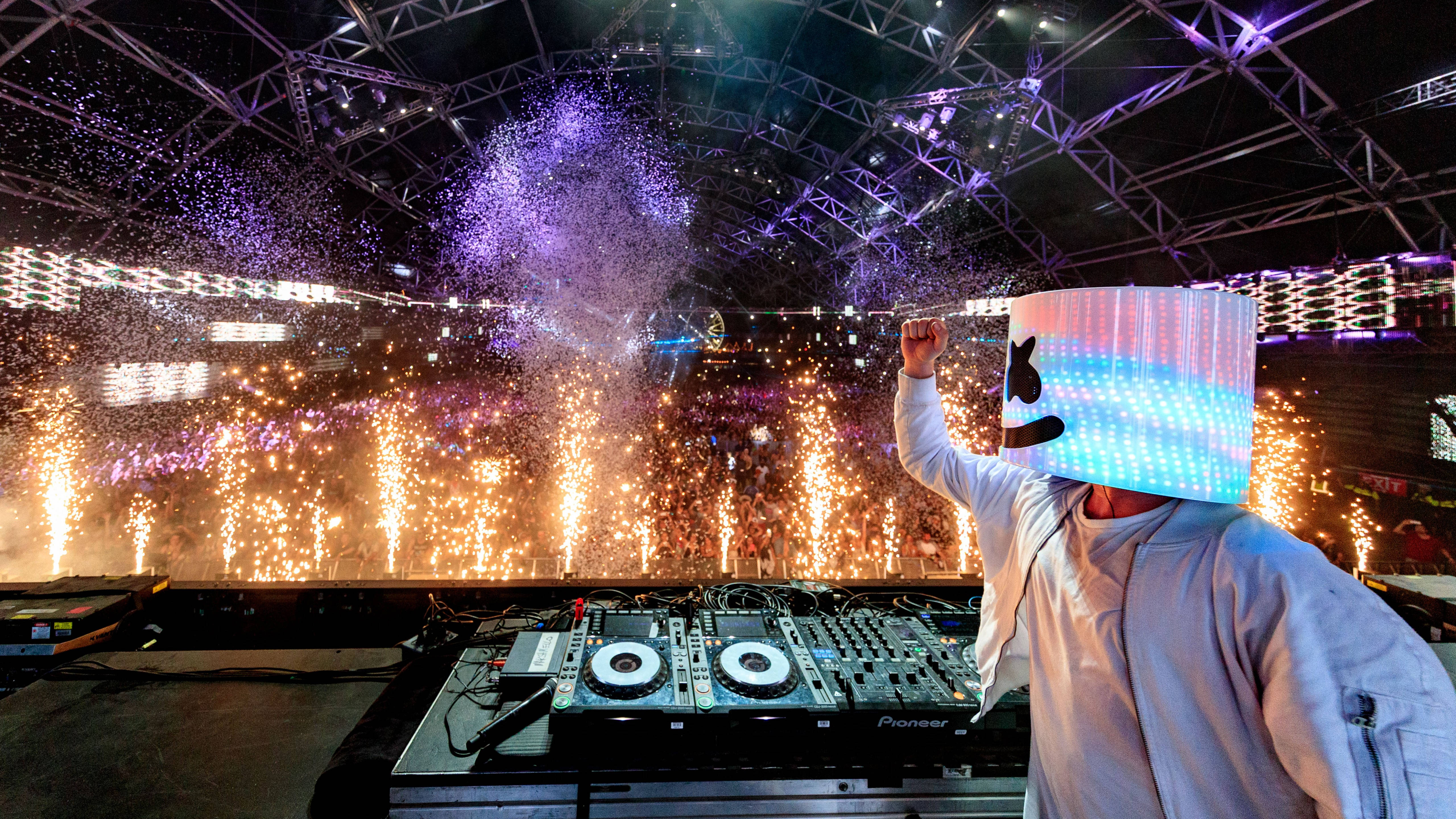 Marshmello 動態圖 桌布 壁紙 — DJ Marshmello 在夜間表演，身後有煙火在鋼結構下爆炸。