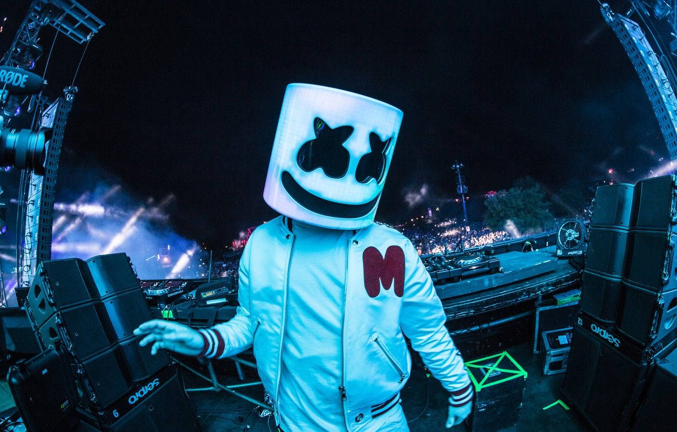Marshmallow Dj 桌布 壁紙 — DJ Marshmello 戴著發光的白色頭盔，在夜晚的霓虹燈光演唱會舞台上表演，身後有群眾和雷射光。