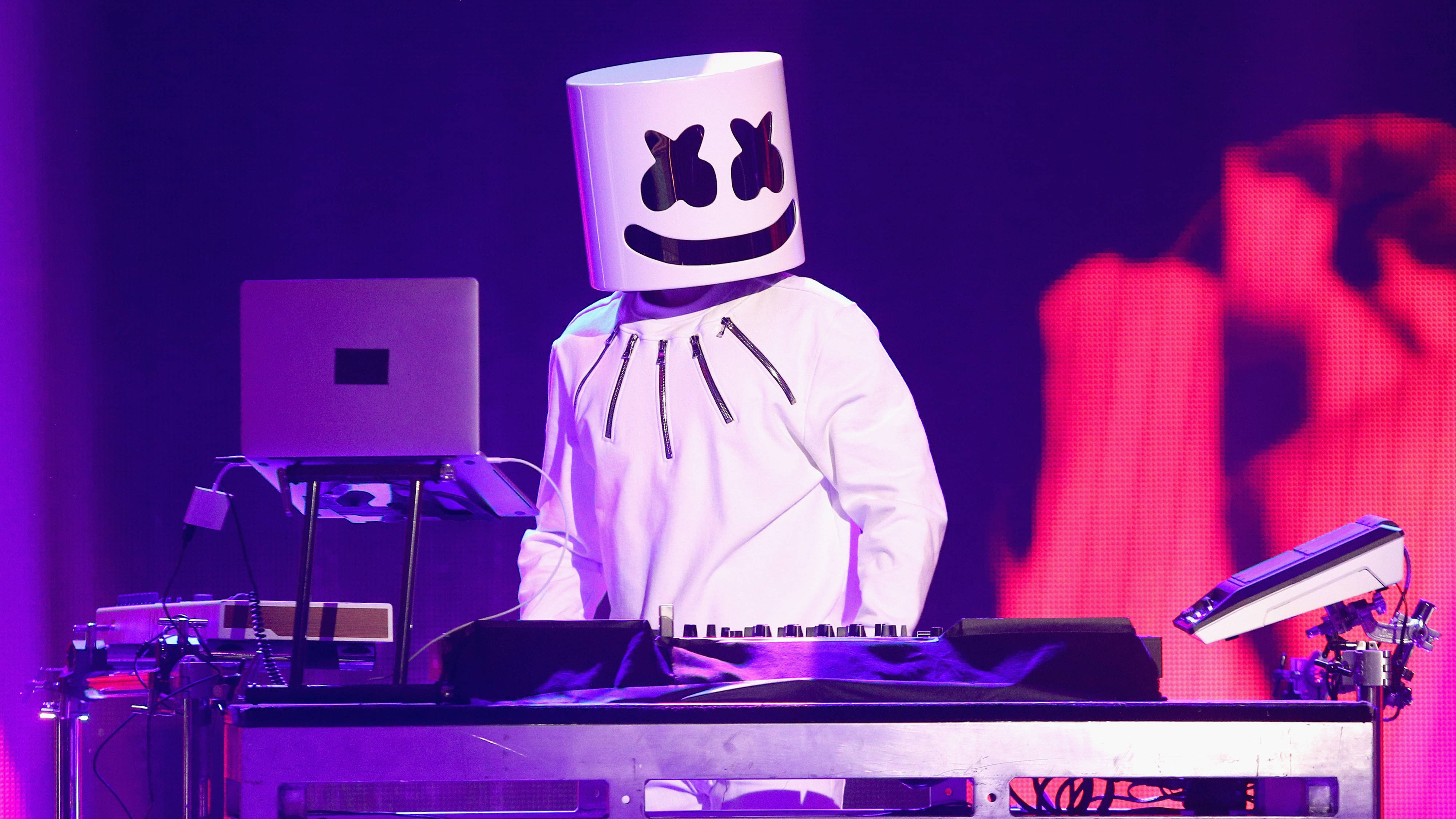 Marshmello 4K 桌布 壁紙 — DJ Marshmello 戴著標誌性白色頭盔，在充滿活力的紫色舞台燈光下，伴隨著發光的設備表演。