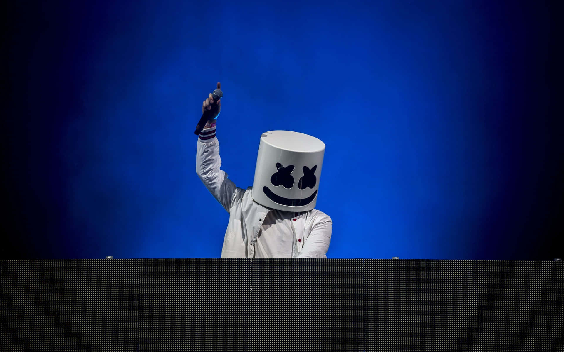 Marshmello 動態圖 桌布 壁紙 — DJ Marshmello 戴著標誌性白色頭盔，在藍色燈光演唱會舞台上舉起手。