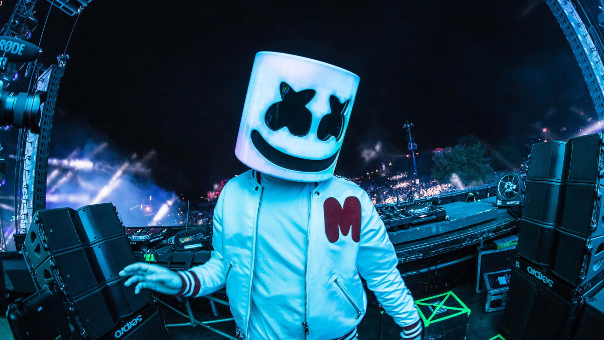 Marshmello 動態圖 桌布 壁紙 — DJ Marshmello 穿著發光白色頭盔和外套，夜晚站在燈光璀璨的音樂會舞台上，背後有群眾和燈光。