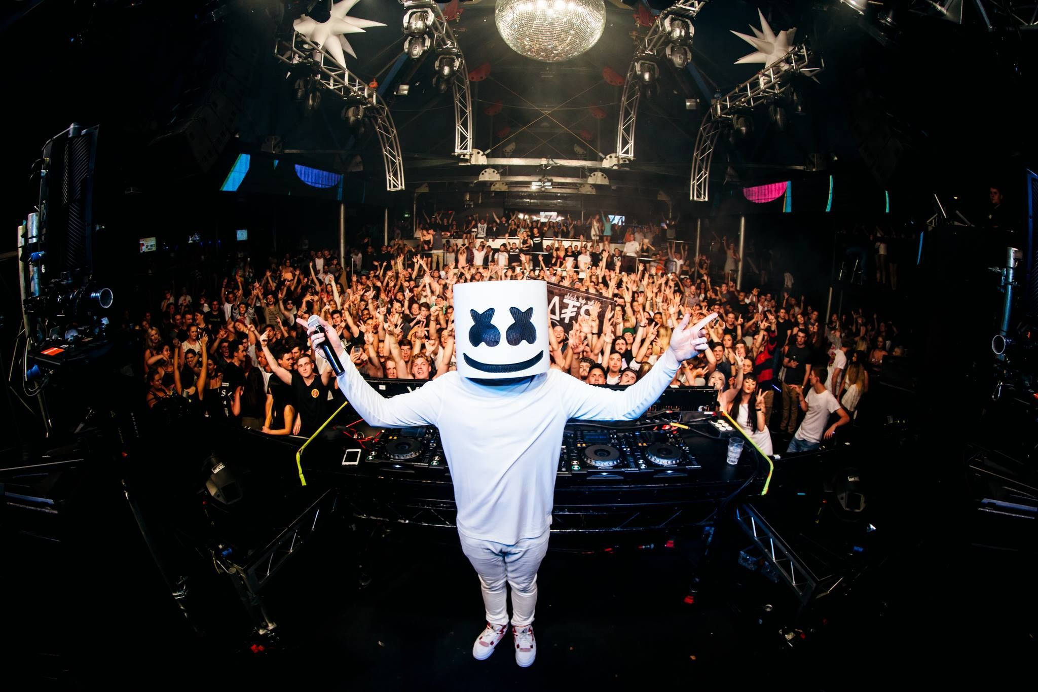 Marshmallow Dj 桌布 壁紙 — DJ Marshmello 身穿白色西裝和頭盔，在迪斯可燈光下，高舉雙臂，在歡呼的人群面前表演。