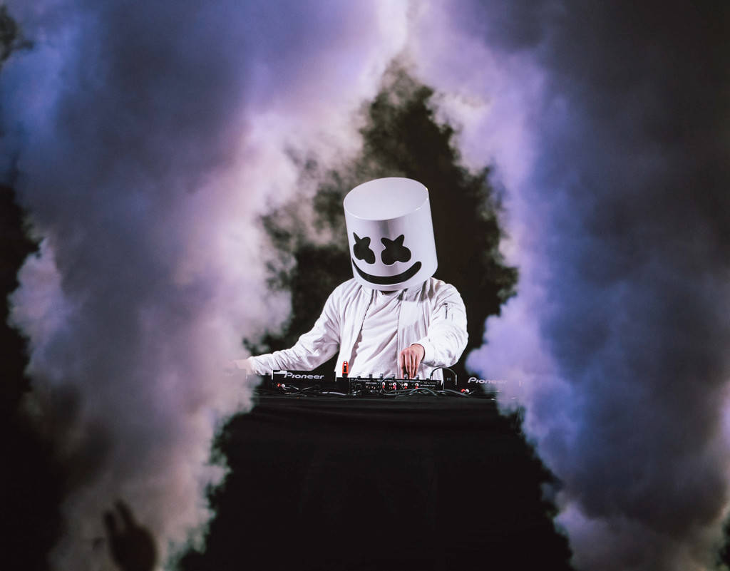 Marshmello 動態圖 桌布 壁紙 — DJ Marshmello 身穿白色西裝和頭盔，在紫色燈光下，於煙霧瀰漫的DJ台後表演。