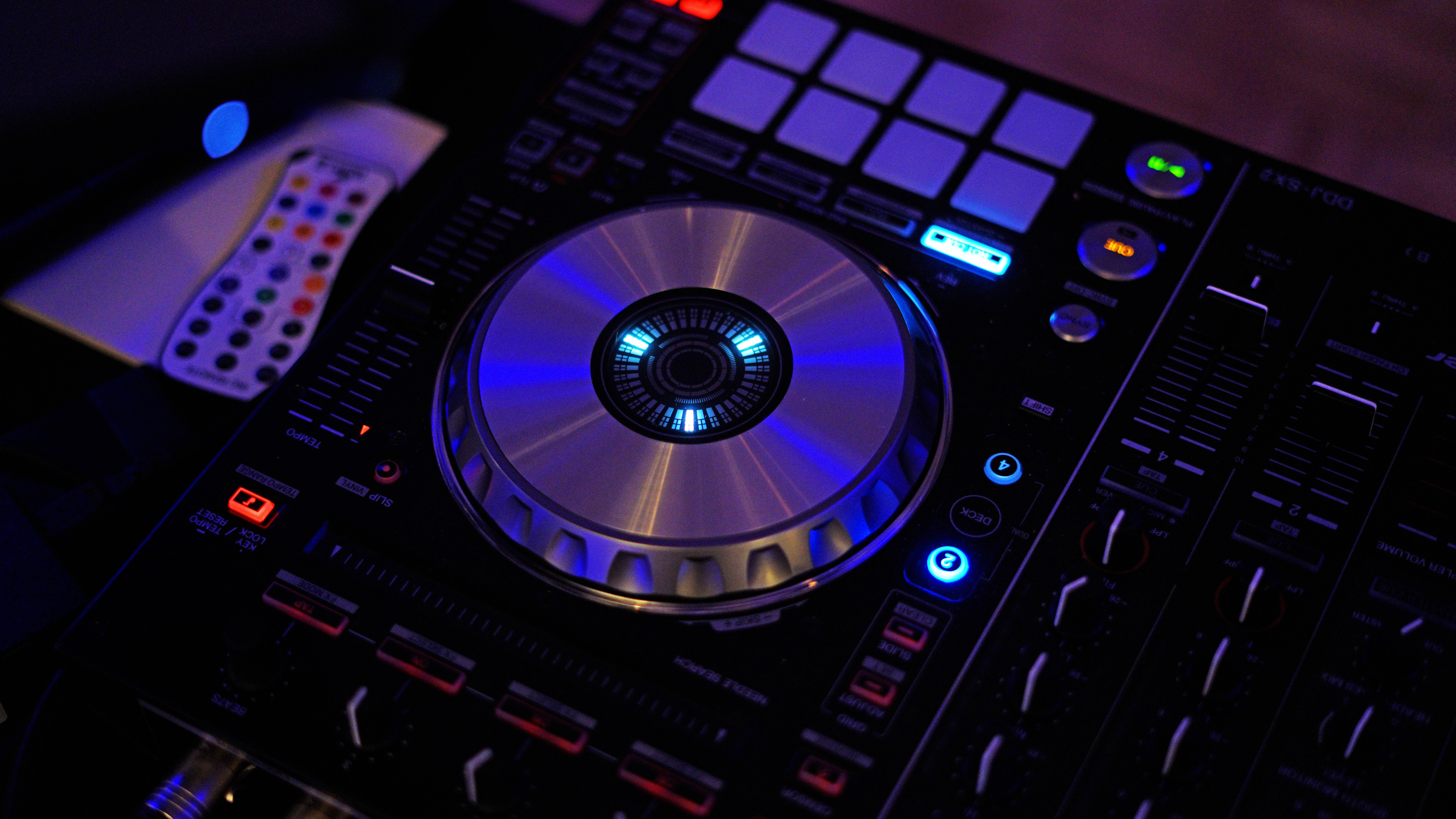 DJ 桌布 壁紙 — DJ 控制器在黑暗的俱樂部環境中發出藍色和紅色光的特寫。