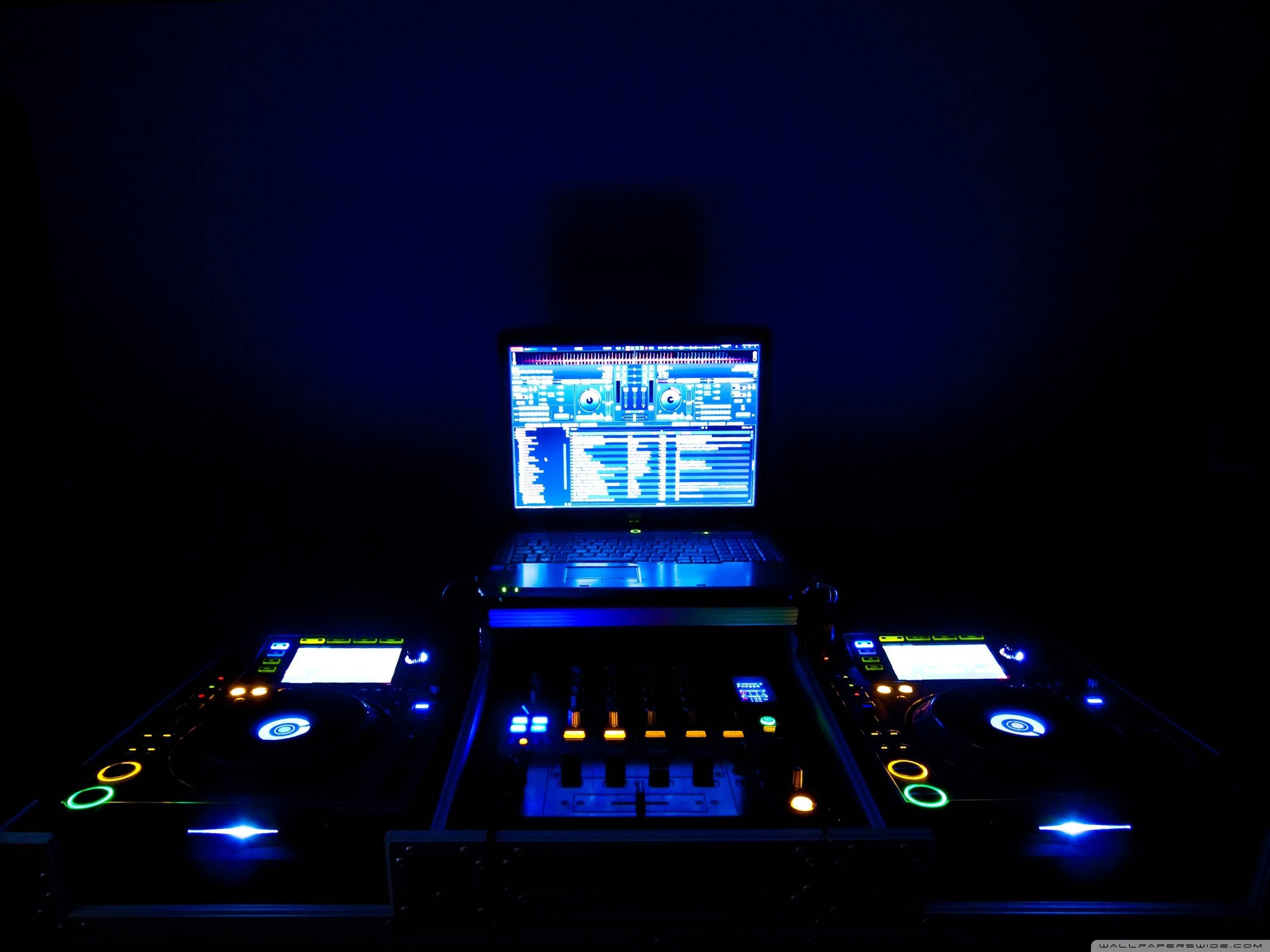 DJ 桌布 壁紙 — DJ 設備在黑暗的房間中發出藍色和橙色光芒，以顯示音樂軟體的筆記型電腦為中心。