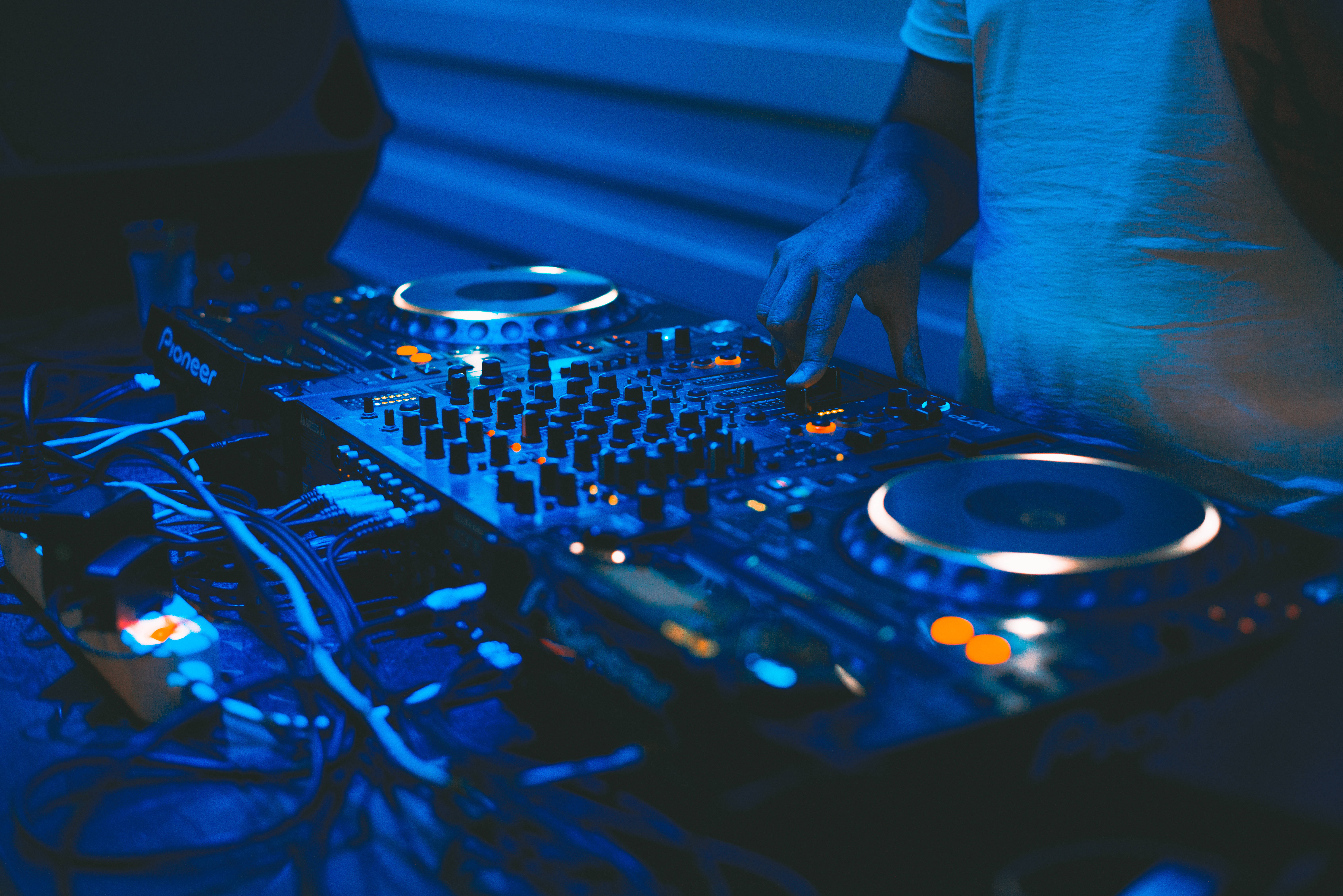 酷炫音樂 桌布 壁紙 — DJ的手正在調整Pioneer混音器上的旋鈕，混音器沐浴在冷藍色舞台燈光和發光的橙色點綴中。