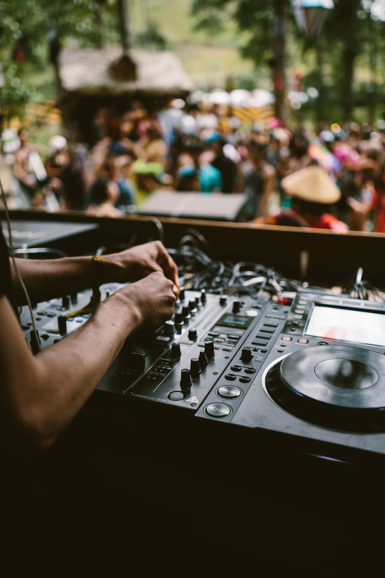 DJ 桌布 壁紙 — DJ的手熟練地在戶外音樂節上操控旋鈕和唱盤，背景是模糊的人群。
