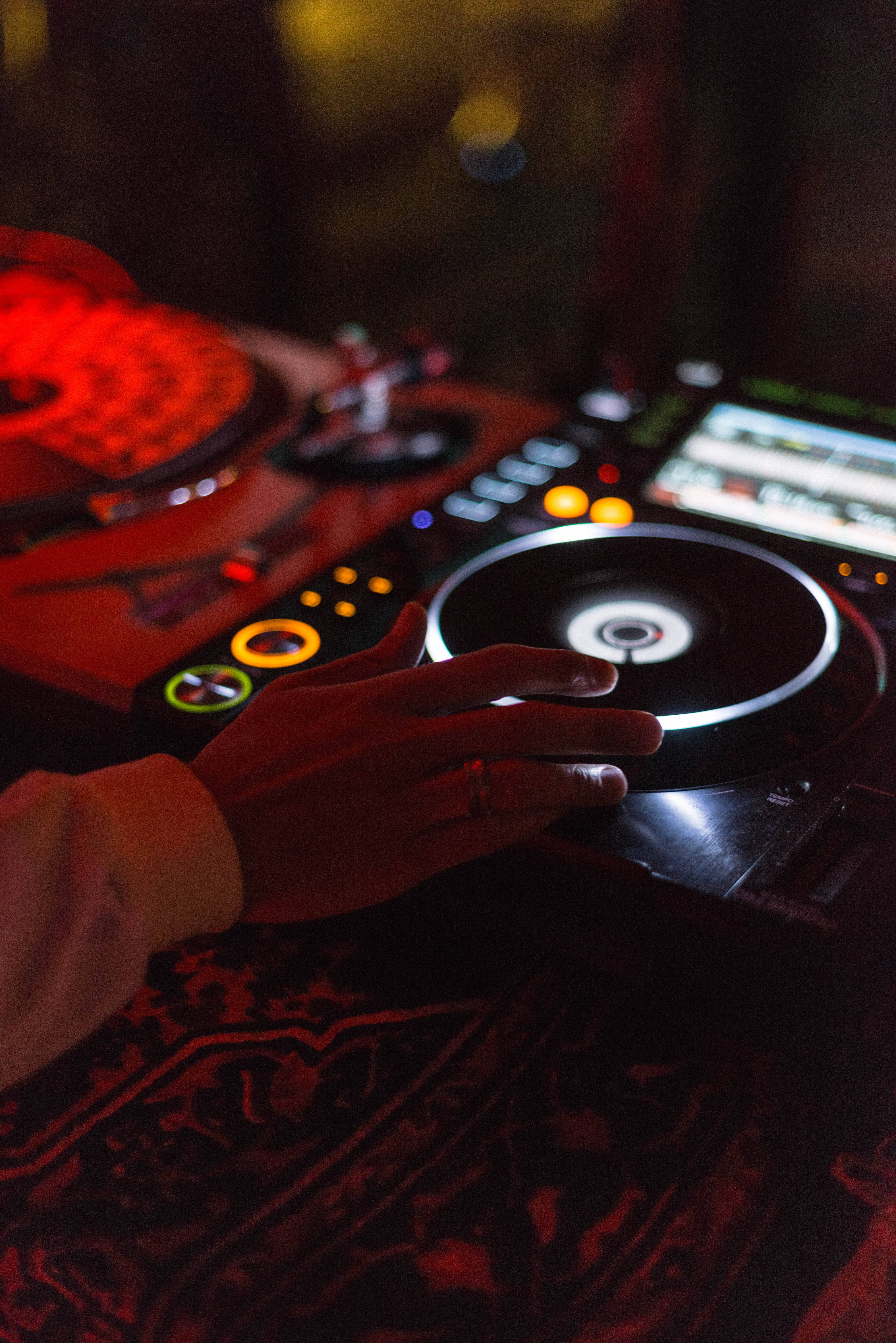 DJ 桌布 壁紙 — DJ的手輕輕放在旋轉的黑膠唱片上，在昏暗的俱樂部中，溫暖的紅色和橙色燈光下。