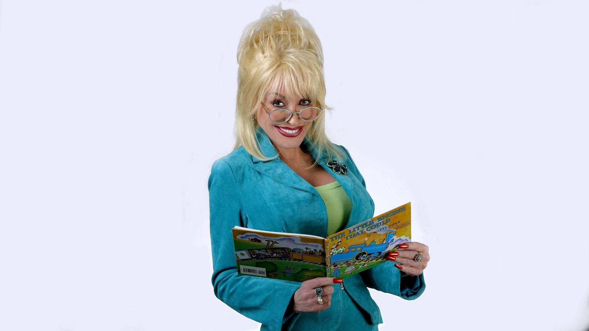dolly 桌布 壁紙 — Dolly Parton 在純白背景前溫暖微笑，手上拿著一本打開的兒童書。