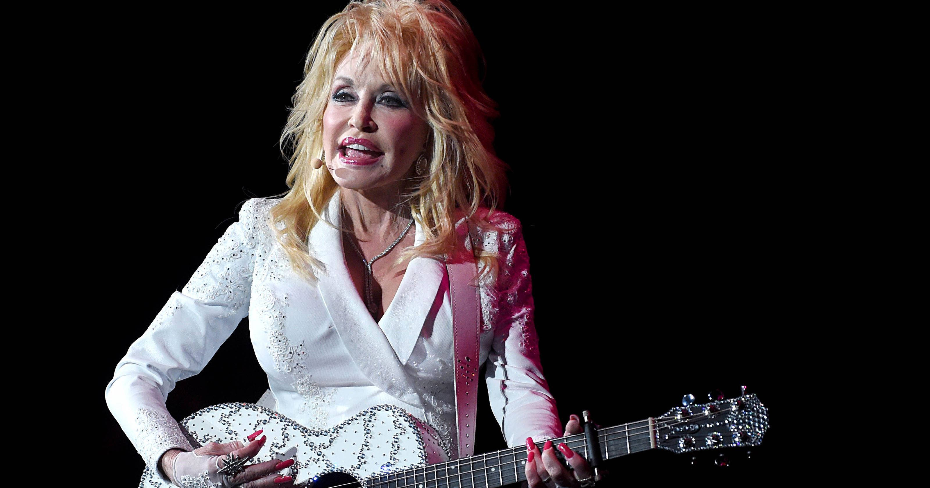 dolly 桌布 壁紙 — Dolly Parton 在黑色背景前，身穿閃亮白色服裝，手持閃爍吉他，在舞台上表演。