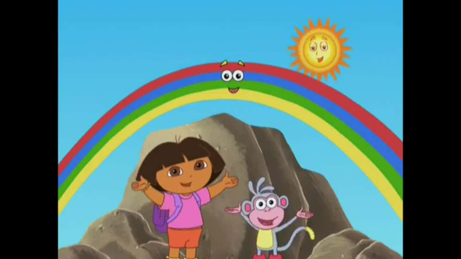 Funny Dora 桌布 壁紙 — Dora 和 Boots 愉快地站在一道微笑的彩虹前，彩虹在明亮的陽光下拱起於岩石地形之上。