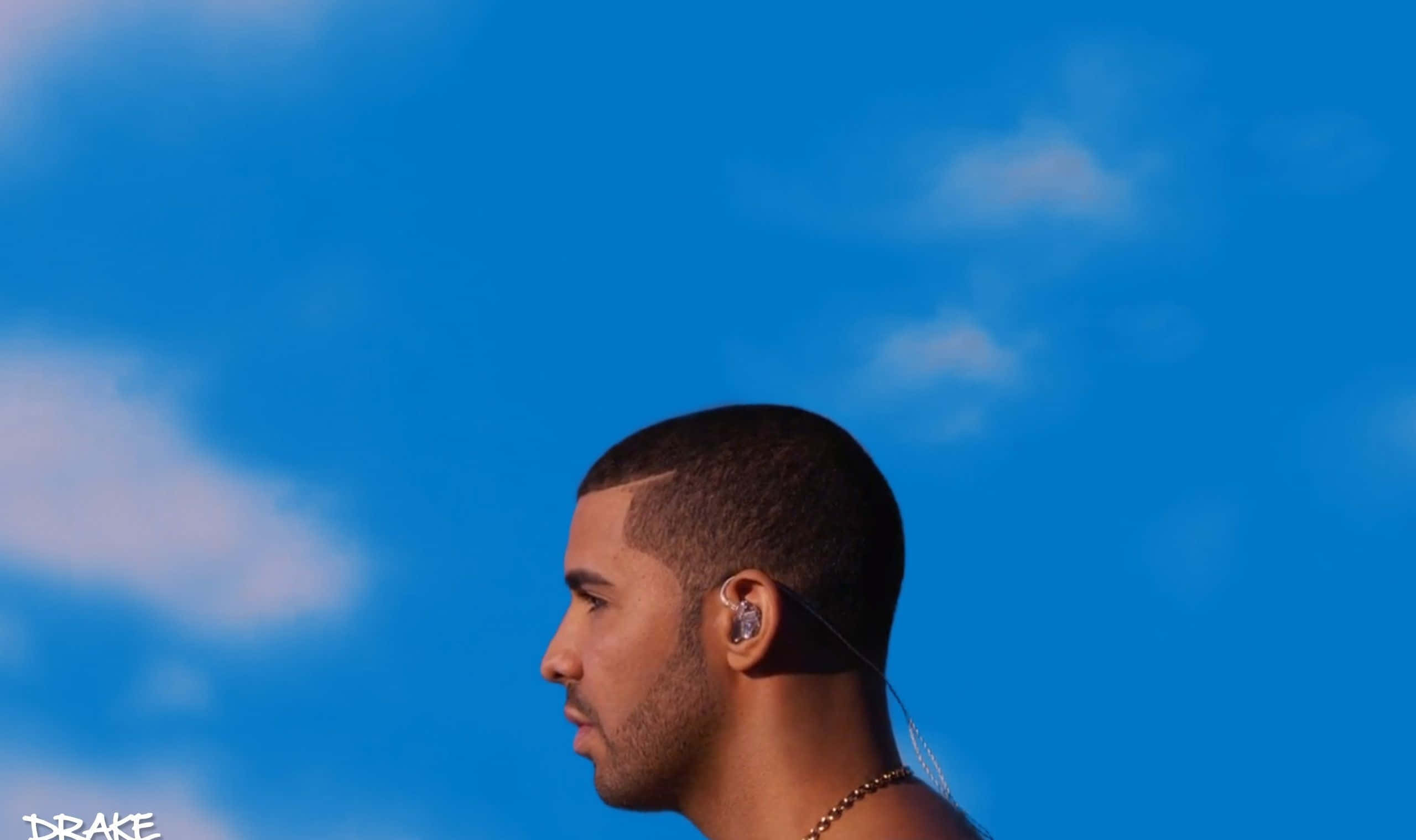 Drake 桌布 壁紙 — Drake 側面照，背景是鮮豔的藍天和柔和的白雲，戴著耳機和金鏈。