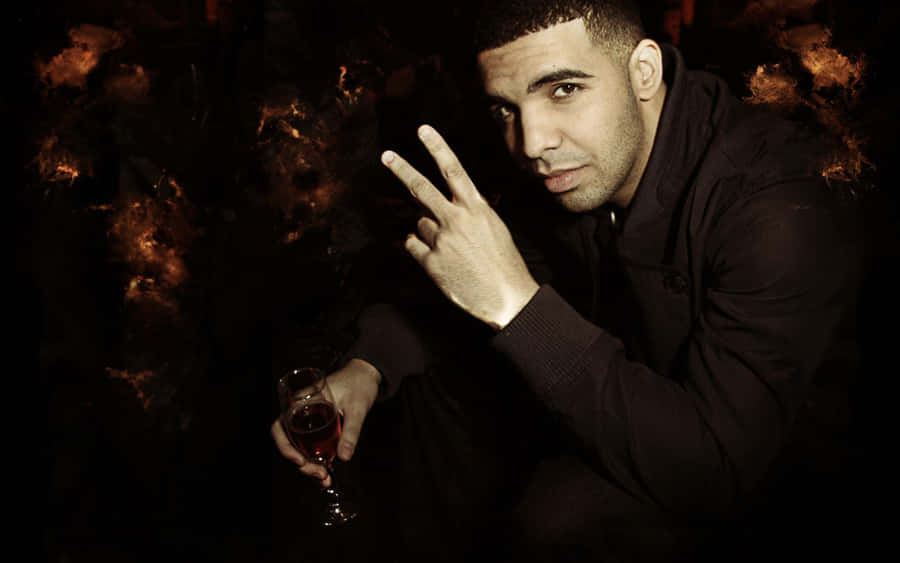 Aesthetic Drake 桌布 壁紙 — Drake 在昏暗的燈光下自信地擺姿勢，手持一杯紅酒並比出和平手勢。