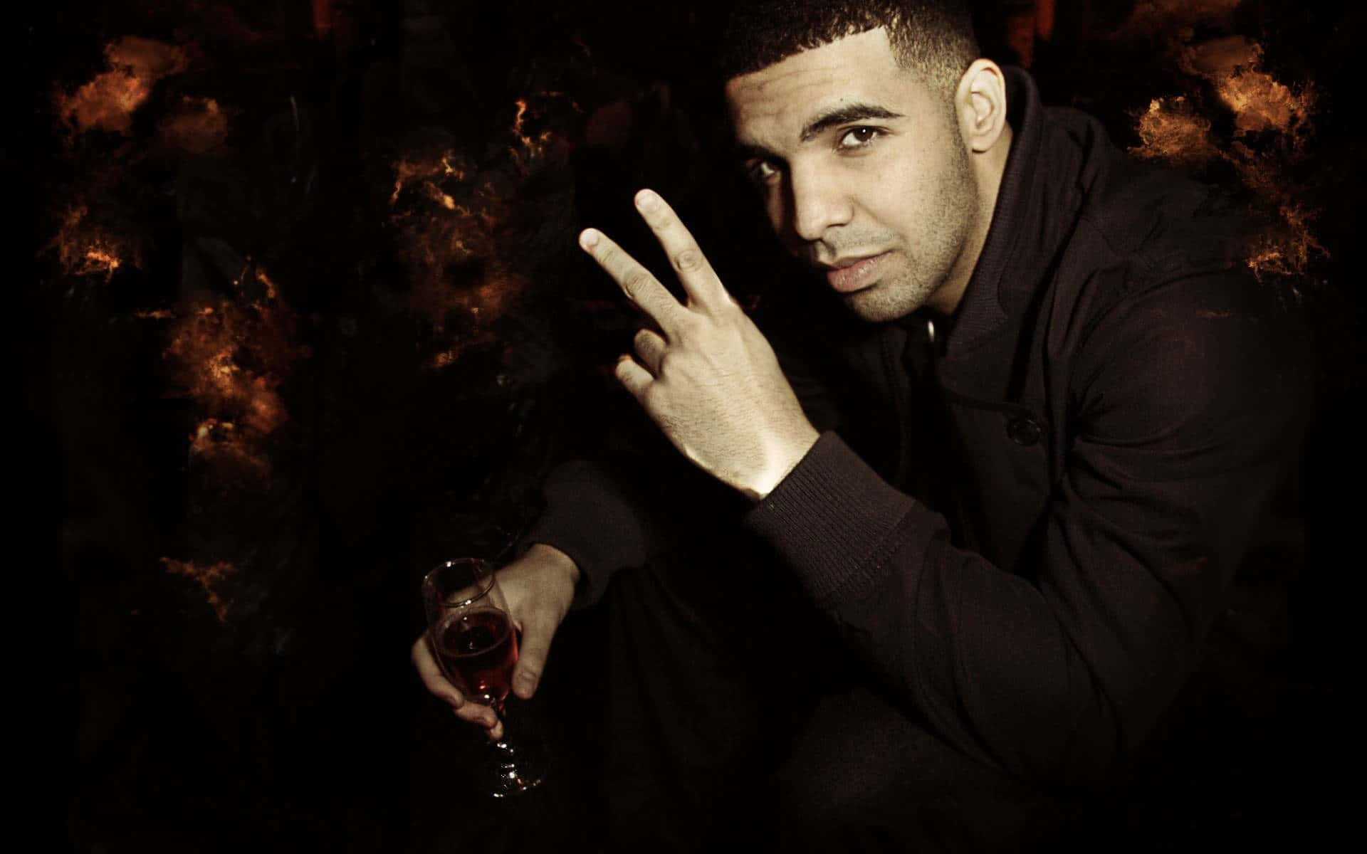 Aesthetic Drake 桌布 壁紙 — Drake 在黑暗環境中自信地擺姿勢，手持一杯紅酒，在戲劇性的燈光下比出和平手勢。