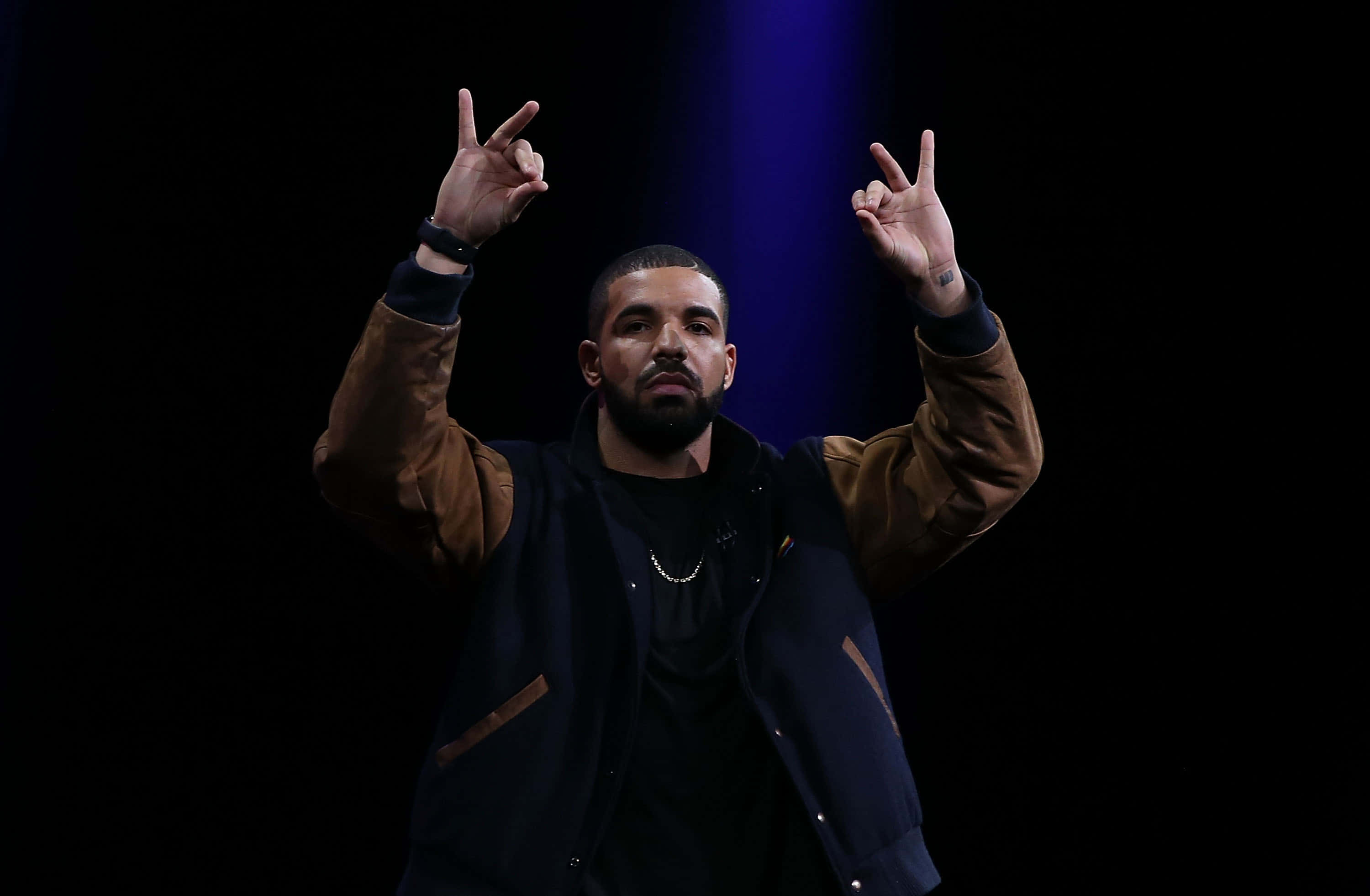 桌布 壁紙 — Drake 在黑色背景前，於藍色聚光燈下站在舞台中央，雙手做出和平手勢。