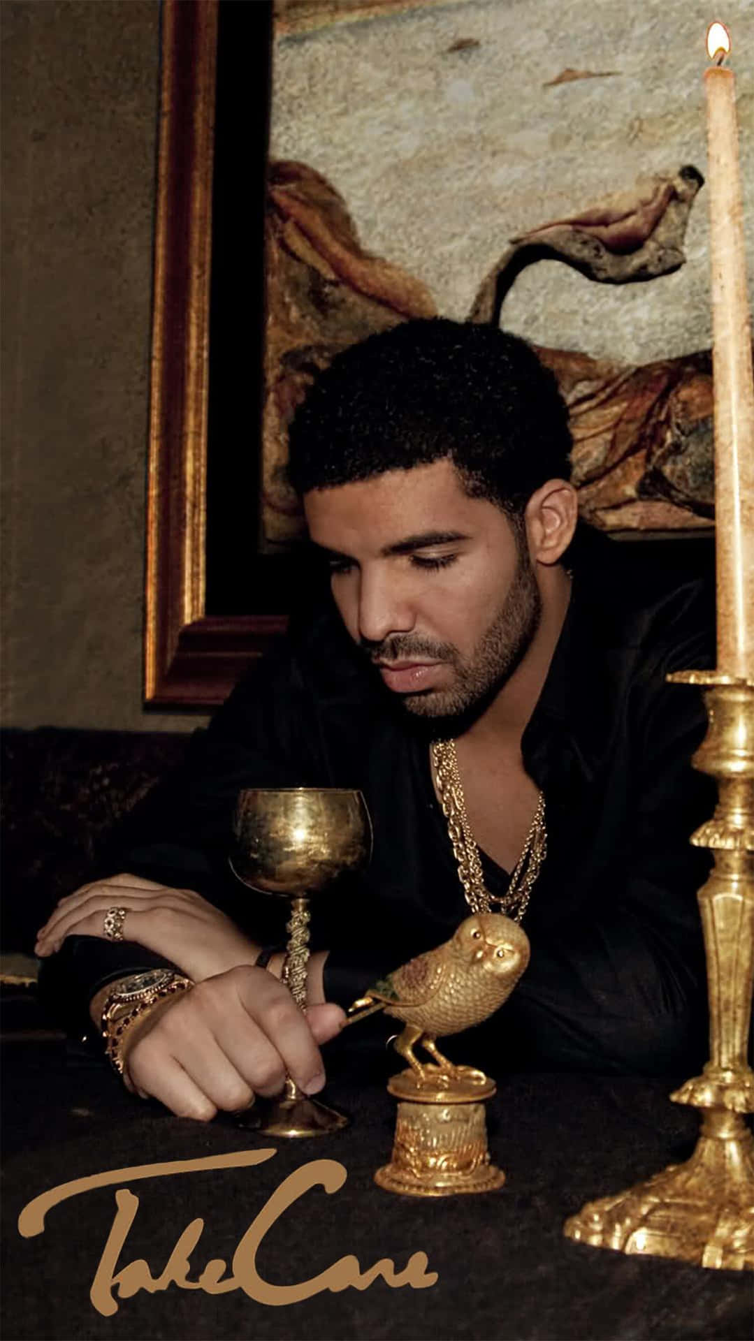 Aesthetic Drake 桌布 壁紙 — Drake 坐在燈光昏暗的房間裡，手持金色高腳杯，旁邊有一根點燃的蠟燭和一個華麗的金色貓頭鷹雕像。