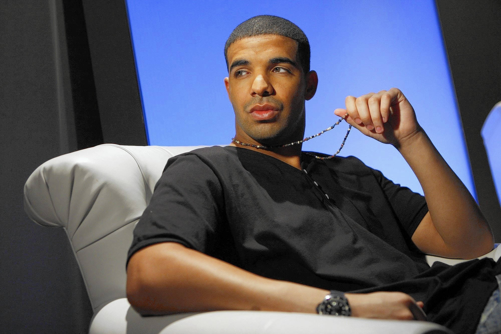 Drake 桌布 壁紙 — Drake 放鬆地坐在白色椅子上，手持珠鏈，背景為藍色。