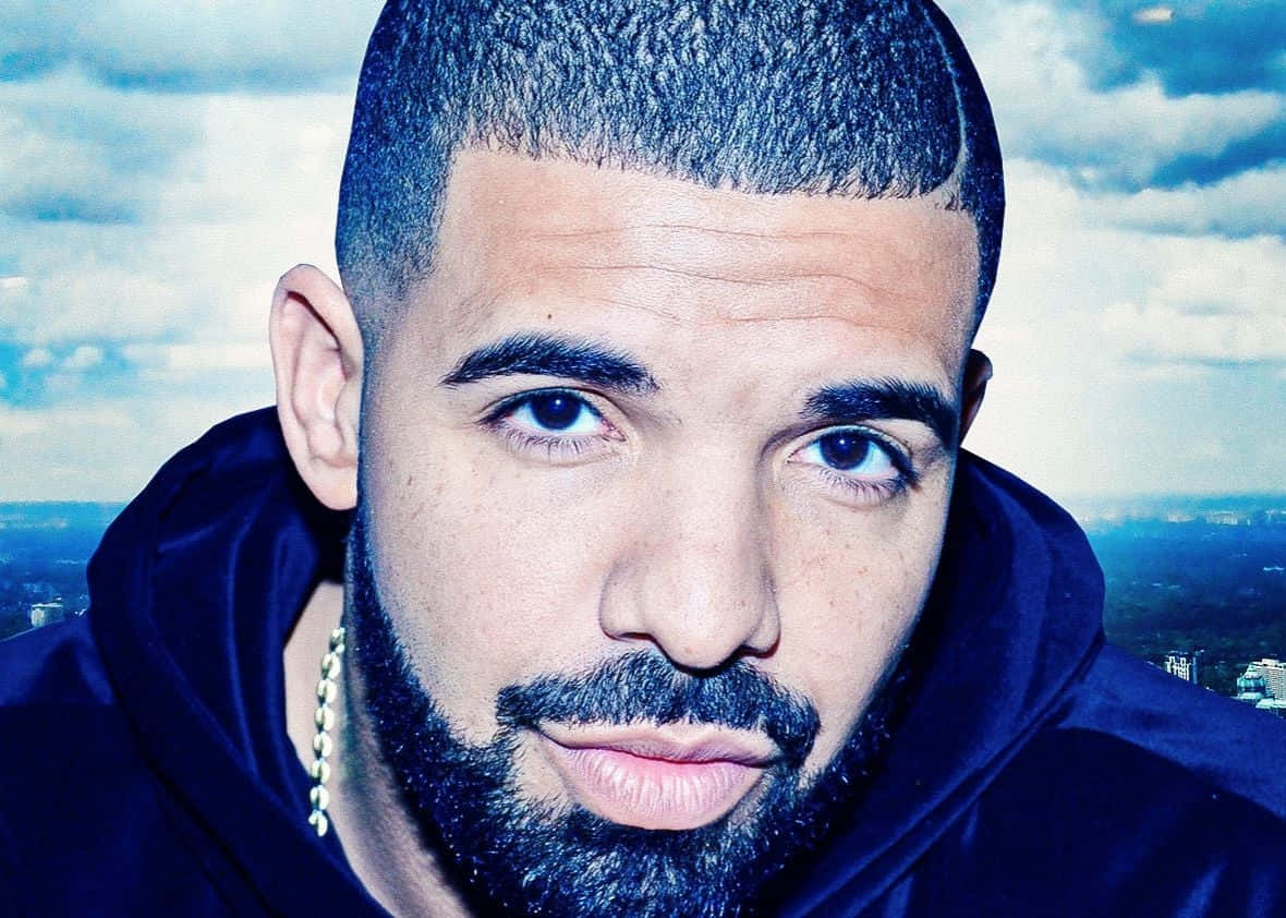 Drake 桌布 壁紙 — Drake 的特寫肖像，表情嚴肅，背景是多雲的天空和遠處的城市景觀。