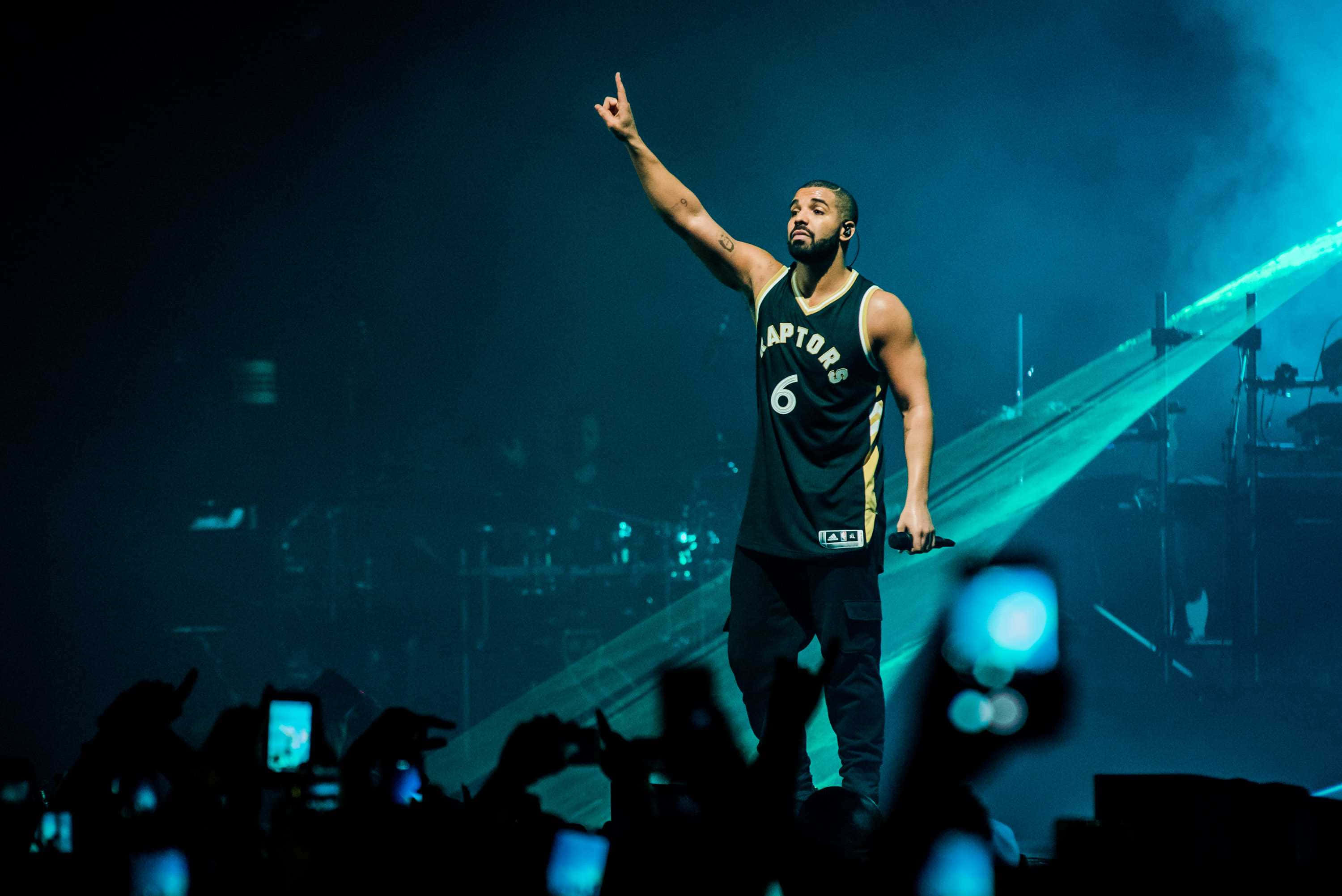 Drake 桌布 壁紙 — Drake 身穿多倫多暴龍隊球衣，在藍色舞台燈光下表演，粉絲在下方錄影。