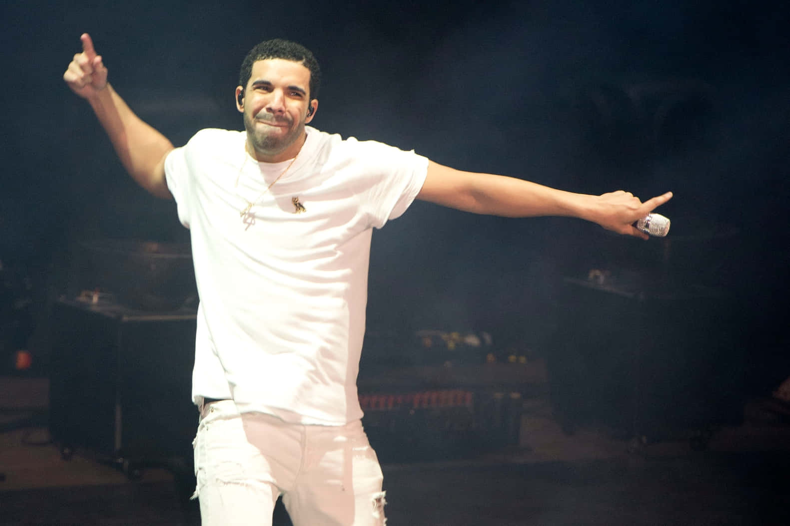 桌布 壁紙 — Drake 身穿白色服裝在舞台上表演，在明亮的舞台燈光下雙臂伸展，身後煙霧繚繞。