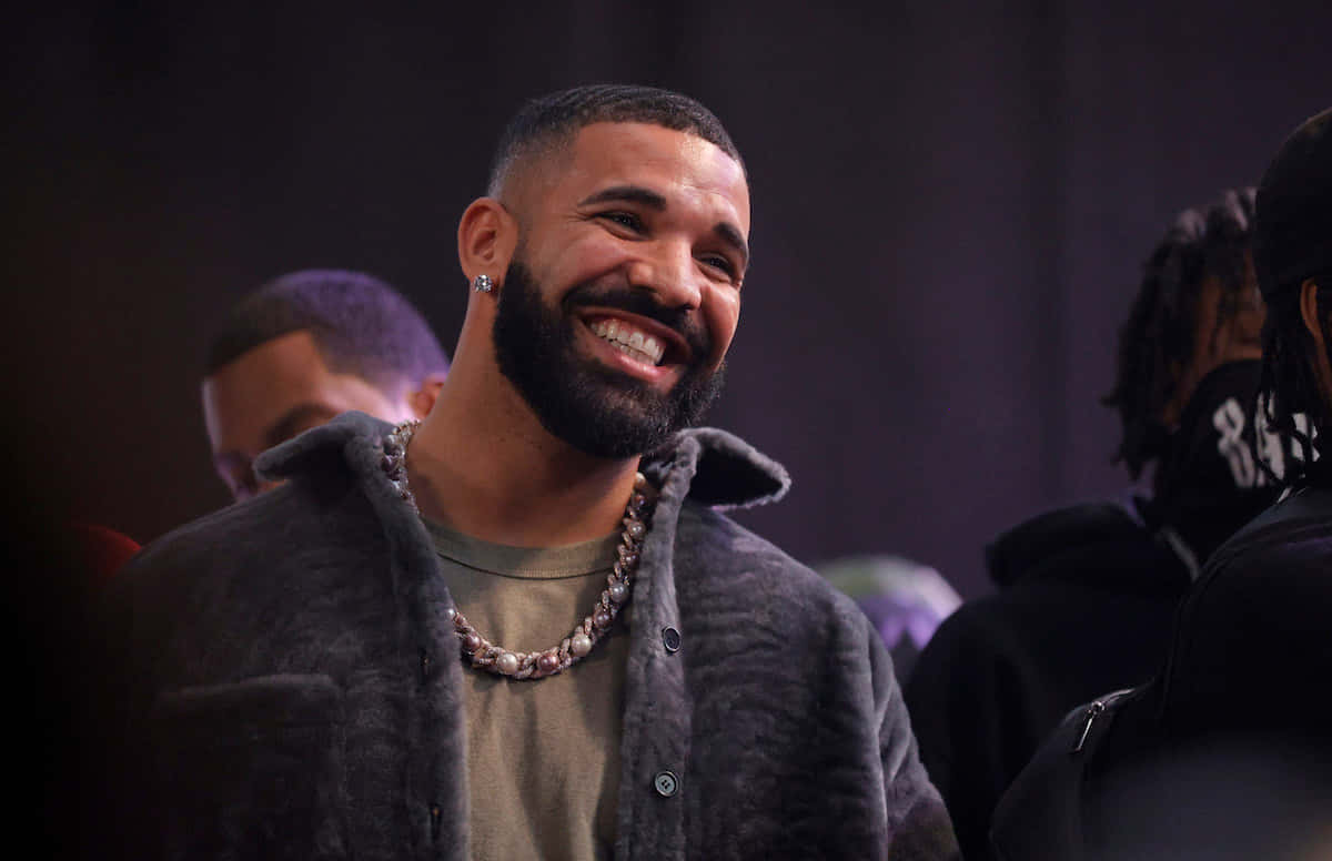 Rap 桌布 壁紙 — Drake 露出燦爛的笑容，身穿質感灰色外套和粗鏈項鍊。