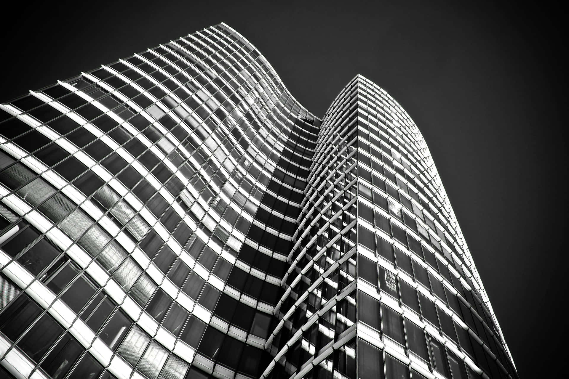  壁紙 — 一張以黑暗天空為背景的現代波浪玻璃摩天大樓的戲劇性低角度黑白照片。