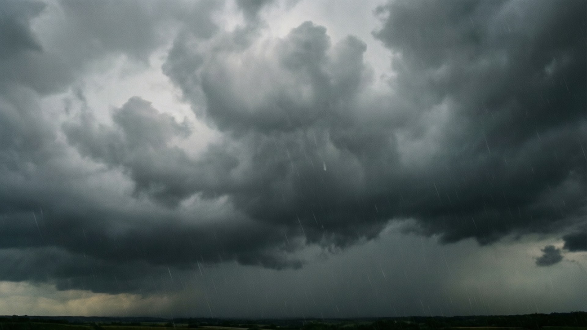 Stormy Gray Clouds 壁紙 — 在陰沉的灰色天空下，一場戲劇性的風暴雲景，大雨落在遙遠的平坦地平線上。