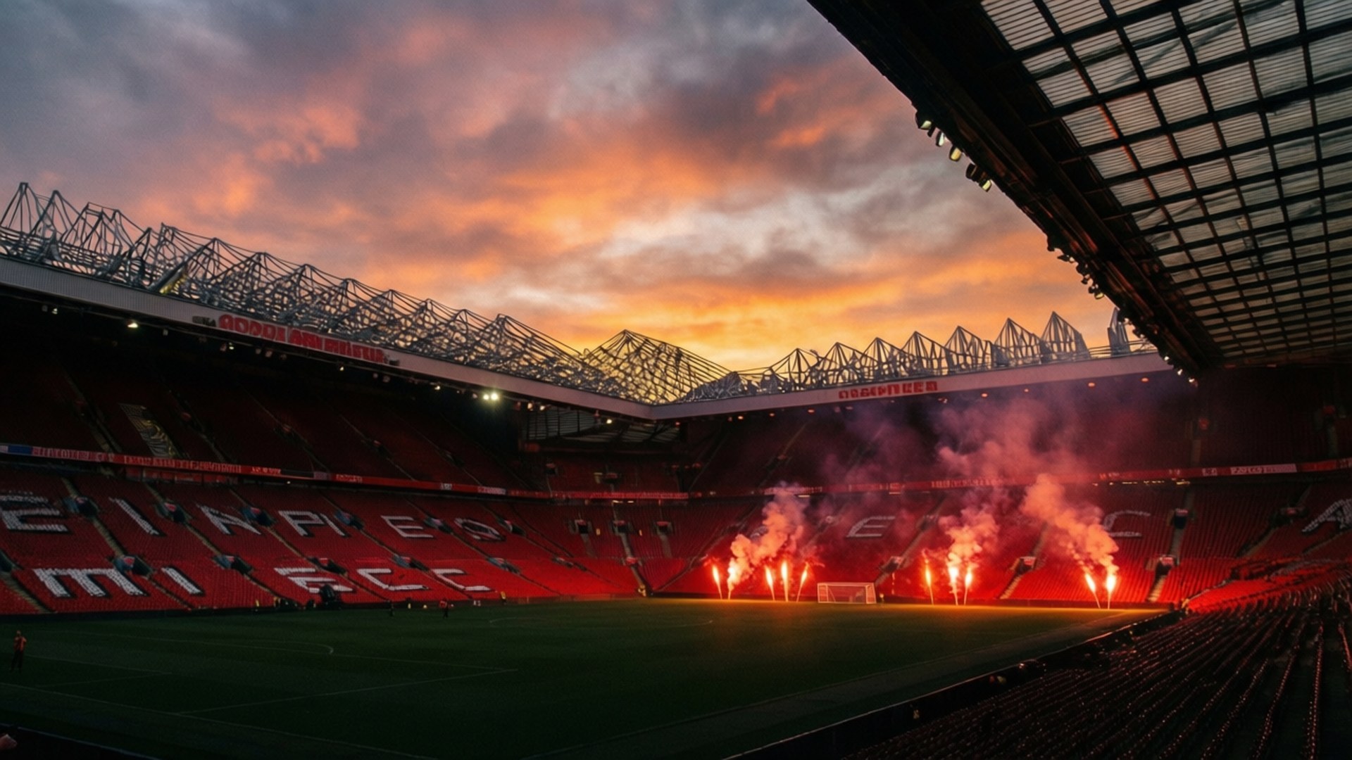 Theatre of Dreams Sunset 壁紙 — 戲劇性的日落將熾熱的橙色和粉紅色色調投射在一個空蕩蕩的足球場上，場內有紅色座位和燃燒的煙火。