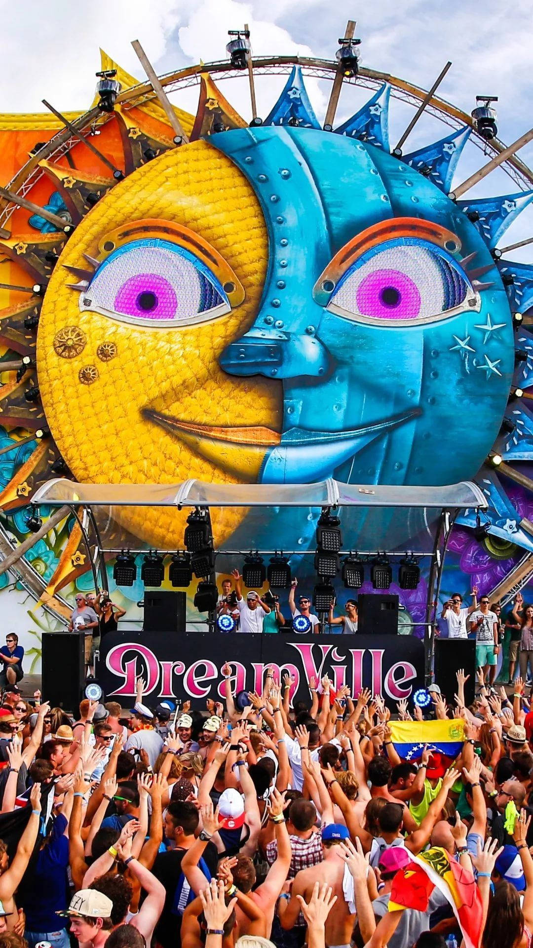 明日世界 桌布 壁紙 — Dreamville 音樂節上一個巨大的太陽和月亮面孔舞台，下方人群在明亮的天空下歡呼。