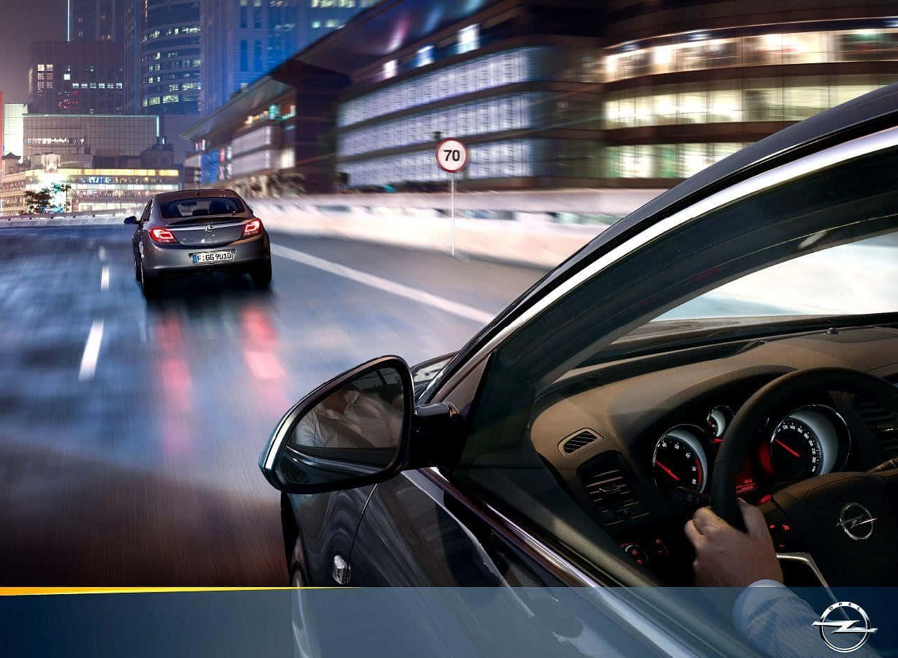 Opel Insignia 桌布 壁紙 — 司機的手緊握著一輛時尚黑色汽車的方向盤，在夜晚霓虹燈閃爍的城市中疾馳，動態模糊的線條掠過。