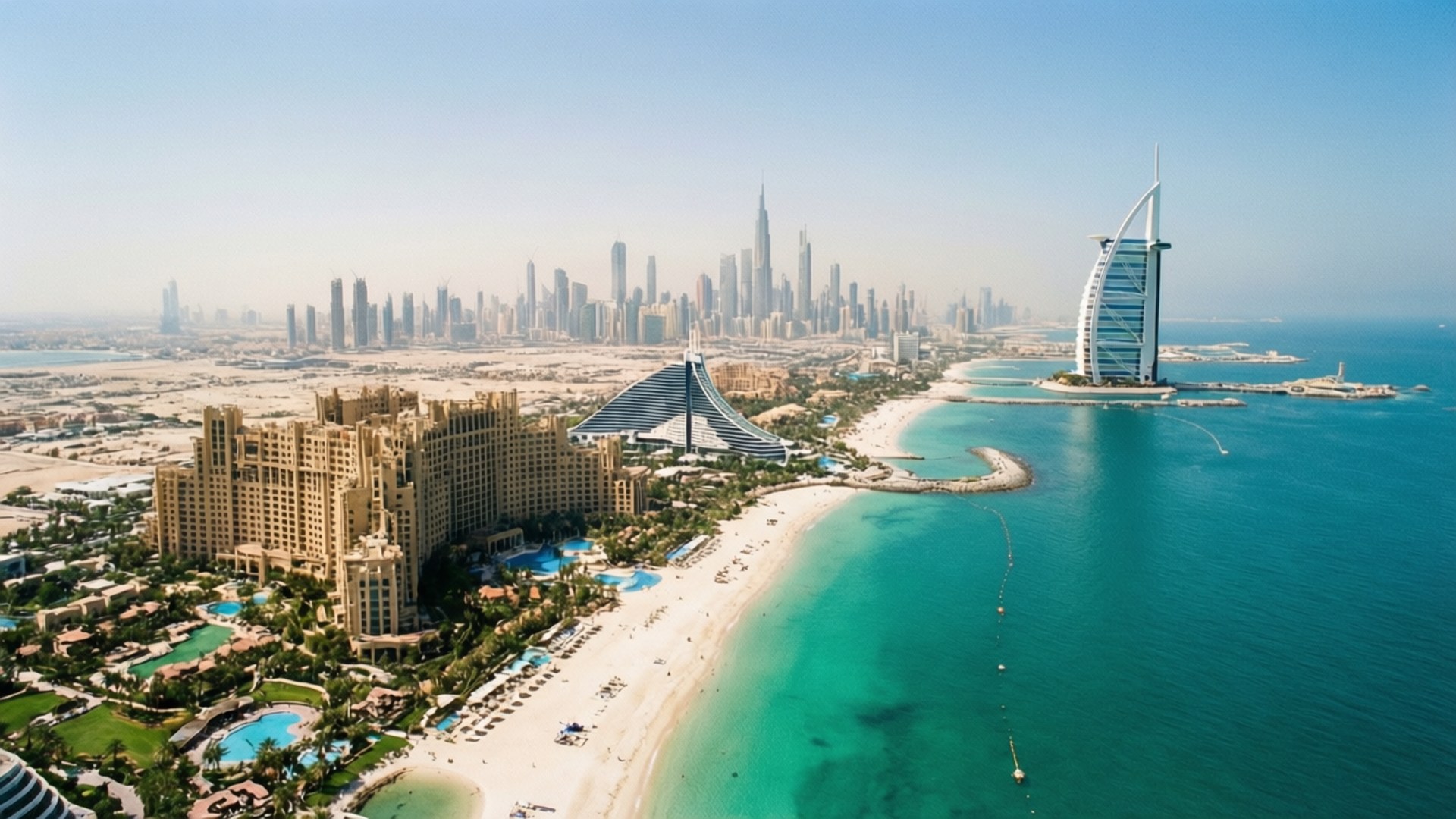 Dubai Coastline Drone 壁紙 — 杜拜海岸線的鳥瞰圖，展示了帆船酒店、碧綠的海水以及城市在晴朗藍天下標誌性的摩天大樓。