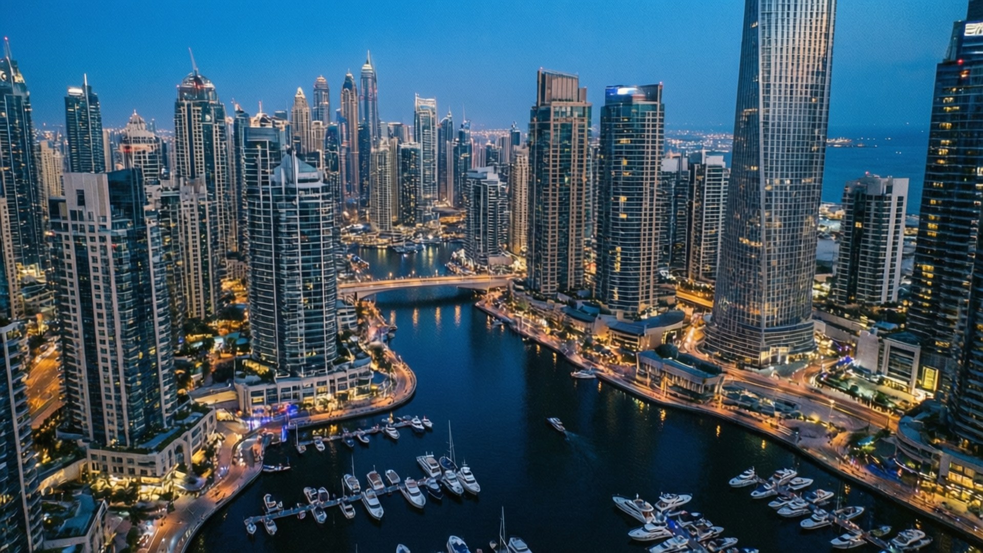 Dubai Marina Blue Hour 壁紙 — 杜拜碼頭黃昏時的鳥瞰圖，發光的摩天大樓倒映在水面上，遊艇沿著彎曲的運河停泊。