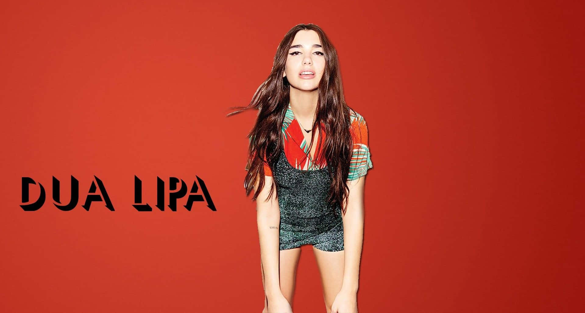 Dua Lipa 桌布 壁紙 — Dua Lipa 自信地站在大膽的紅色背景前，身穿彩色圖案上衣和閃亮短褲。
