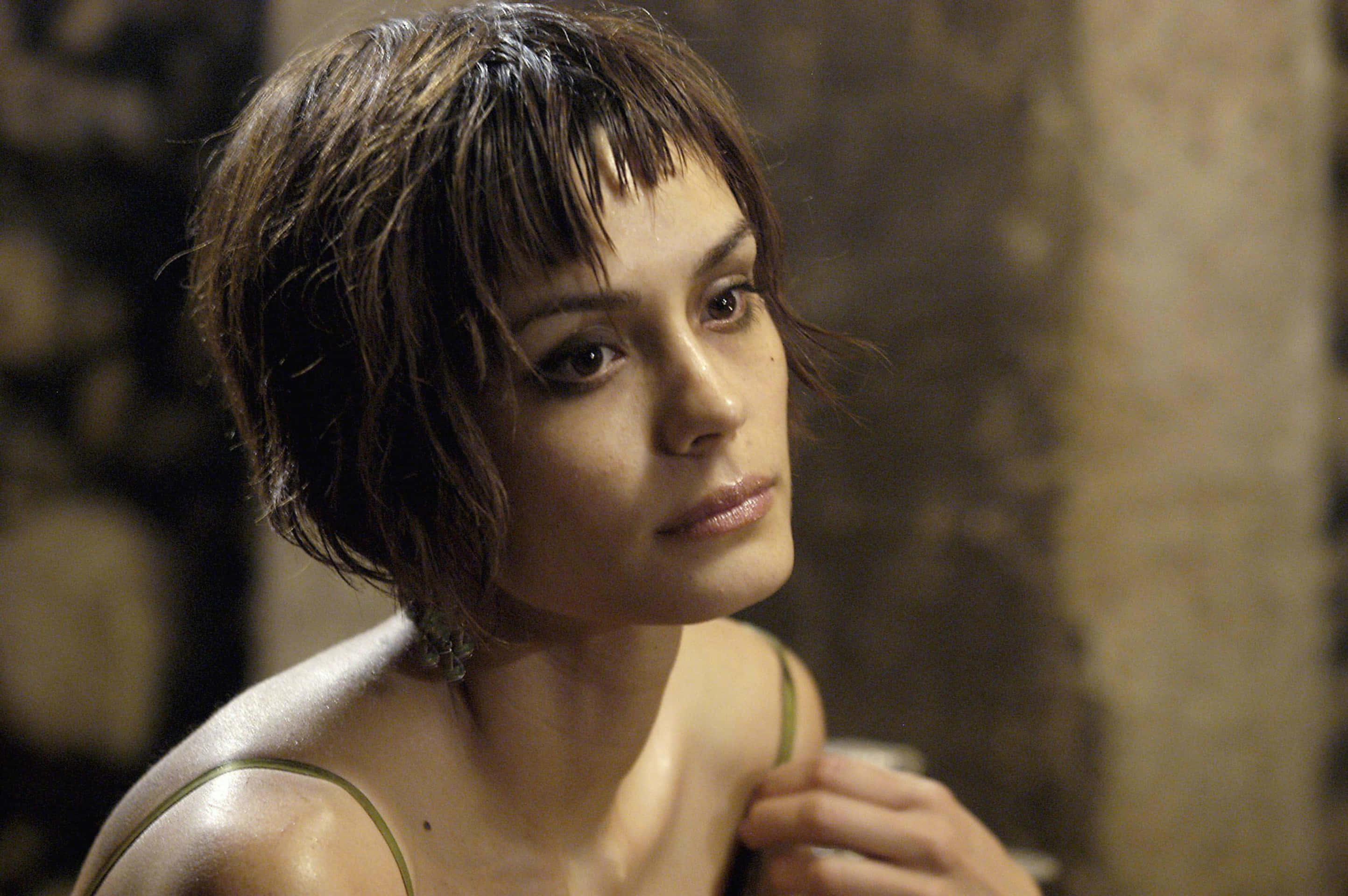 Shannyn Sossamon 桌布 壁紙 — 一位短濕髮的女性在光線昏暗的石牆房間裡若有所思地凝視著。